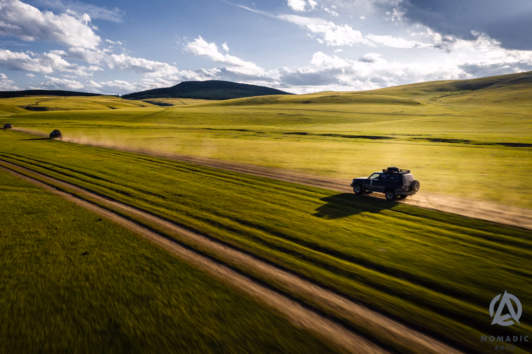 Three 4WD vehicles crossing the green Mongolian steppe.