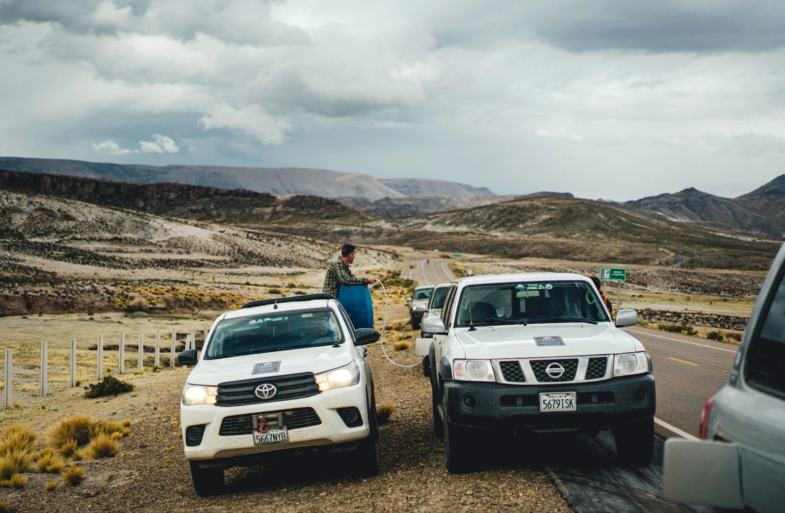 White overlanding pickup truck and SUV stopped on a mountain road in Bolivia for a manual fuel transfer.