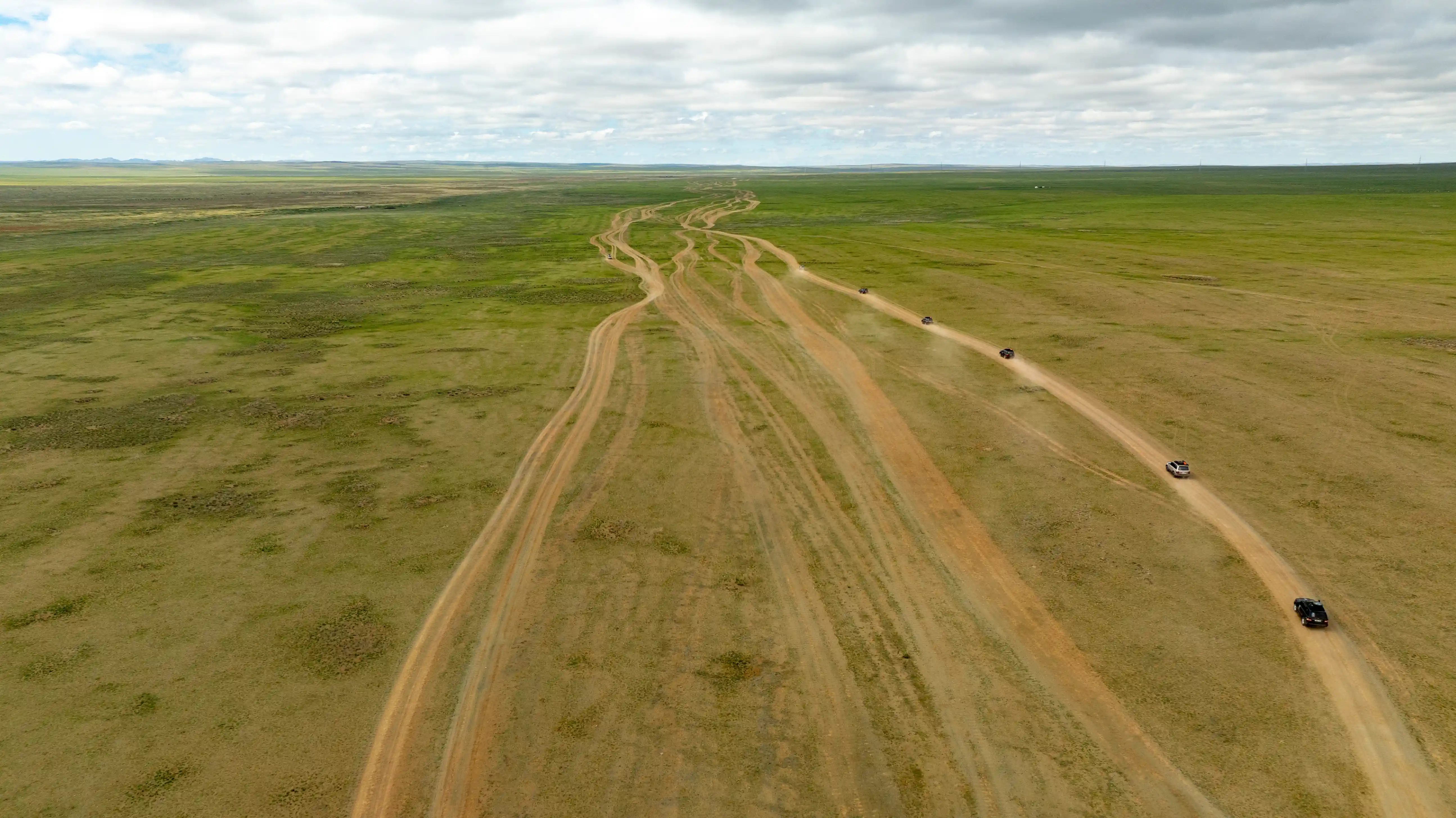 A convoy of cars driving along parallel dirt tracks across the wide open grassland.