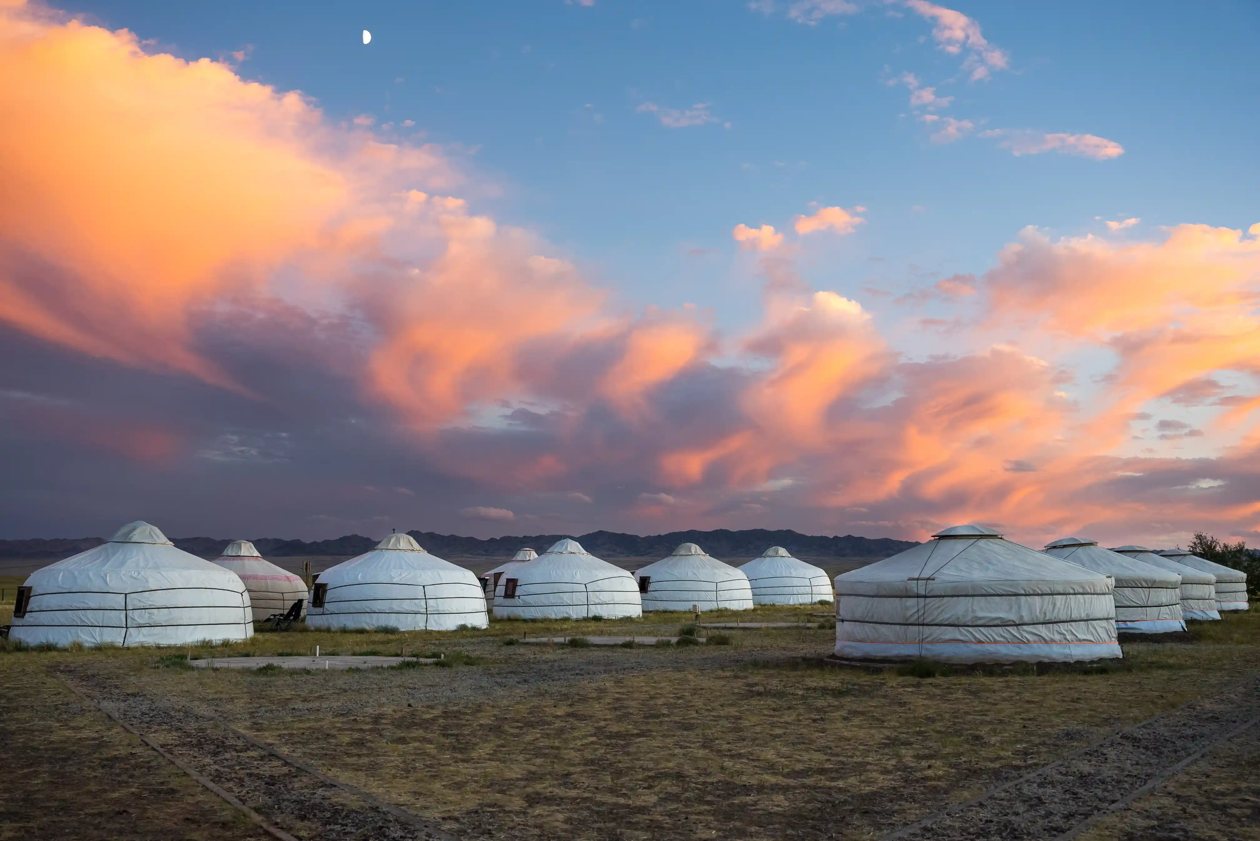 Traditional Mongolian gers beneath a colourful sunset sky on the open Mongolian steppe