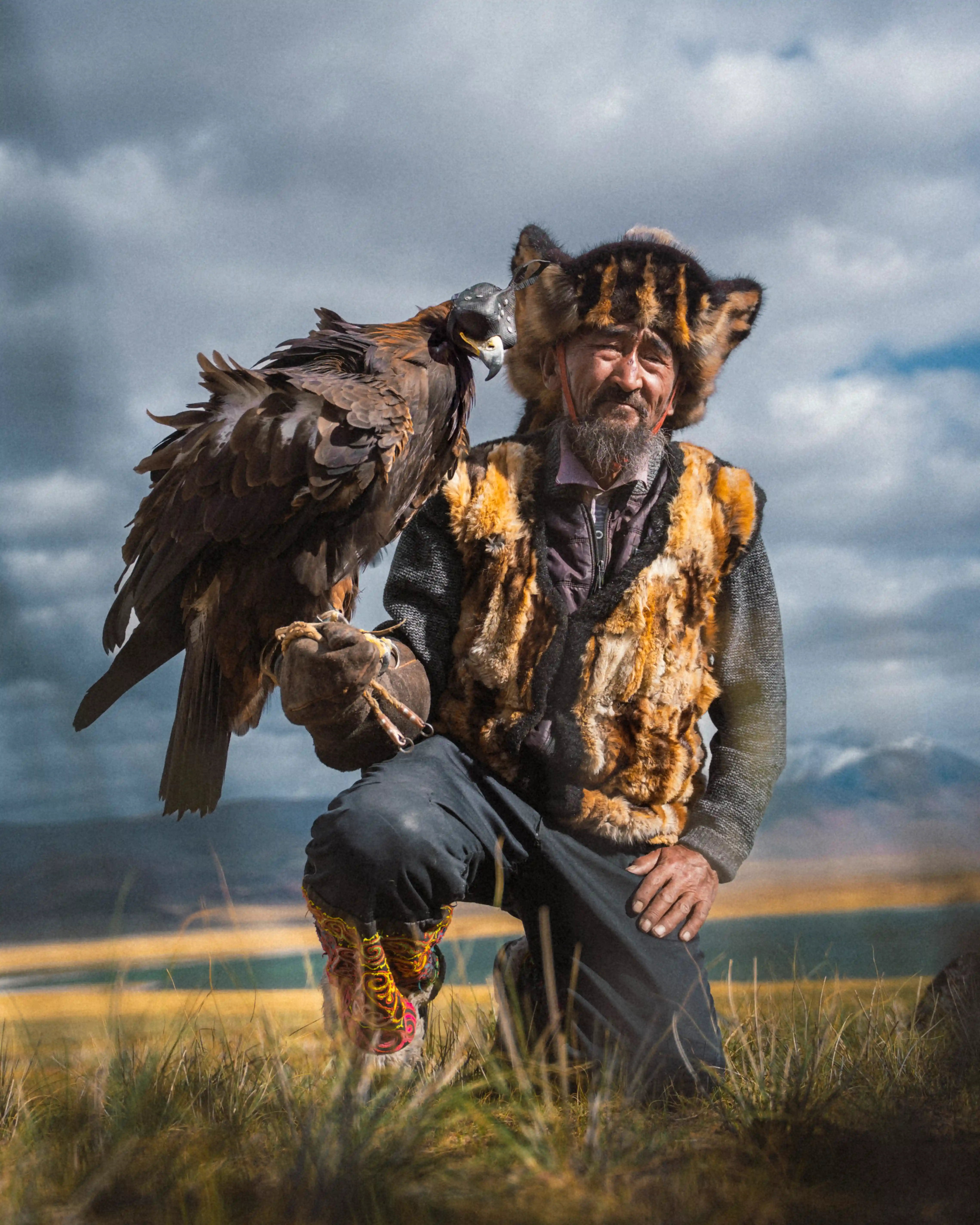 Traditional Kazakh eagle hunter holding a golden eagle on the Mongolian steppe beneath dramatic clouds