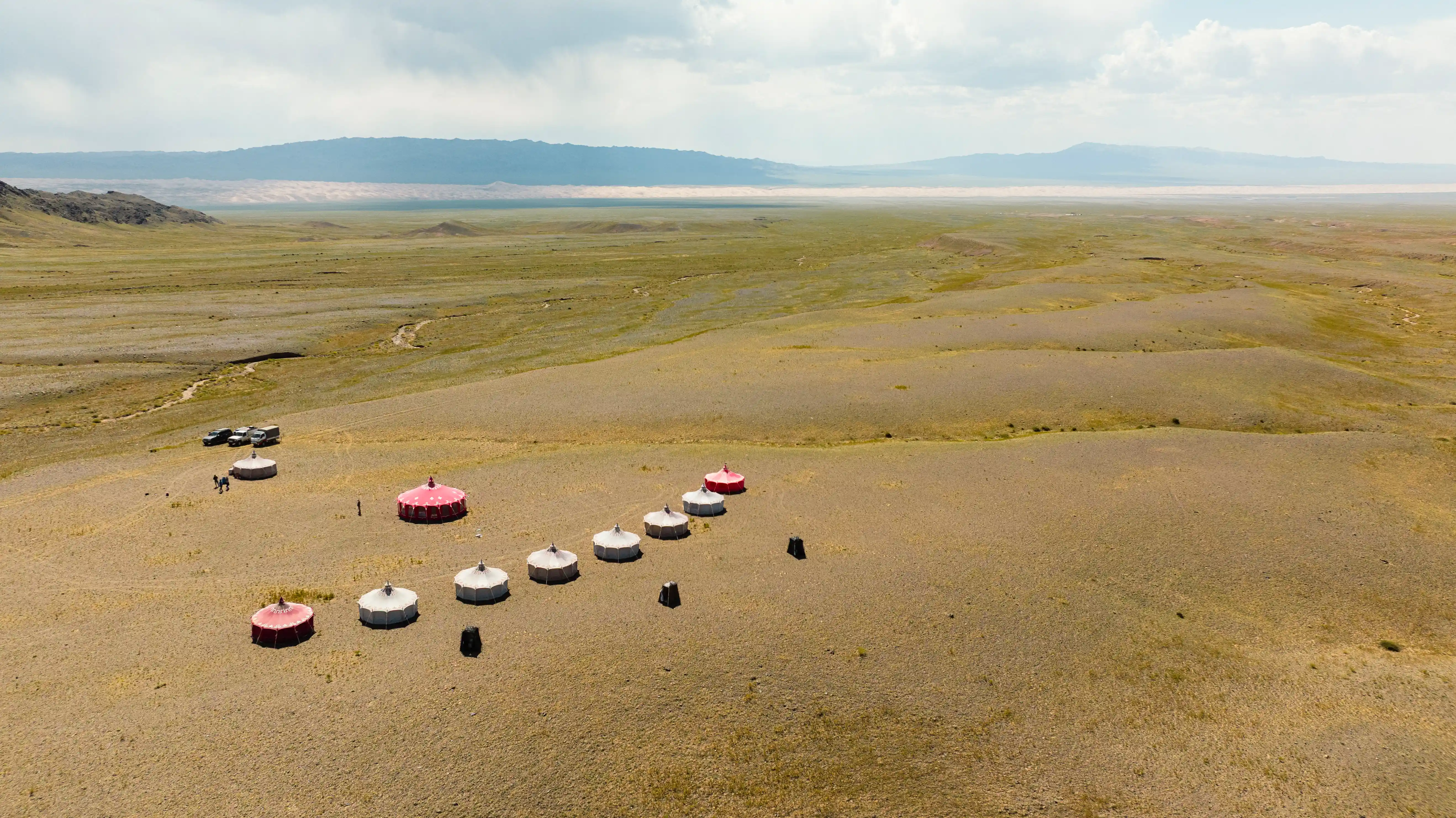 Aerial view of a remote glamping camp with traditional Mongolian yurts surrounded by vast steppe landscapes during a Nomadic Road overland expedition.