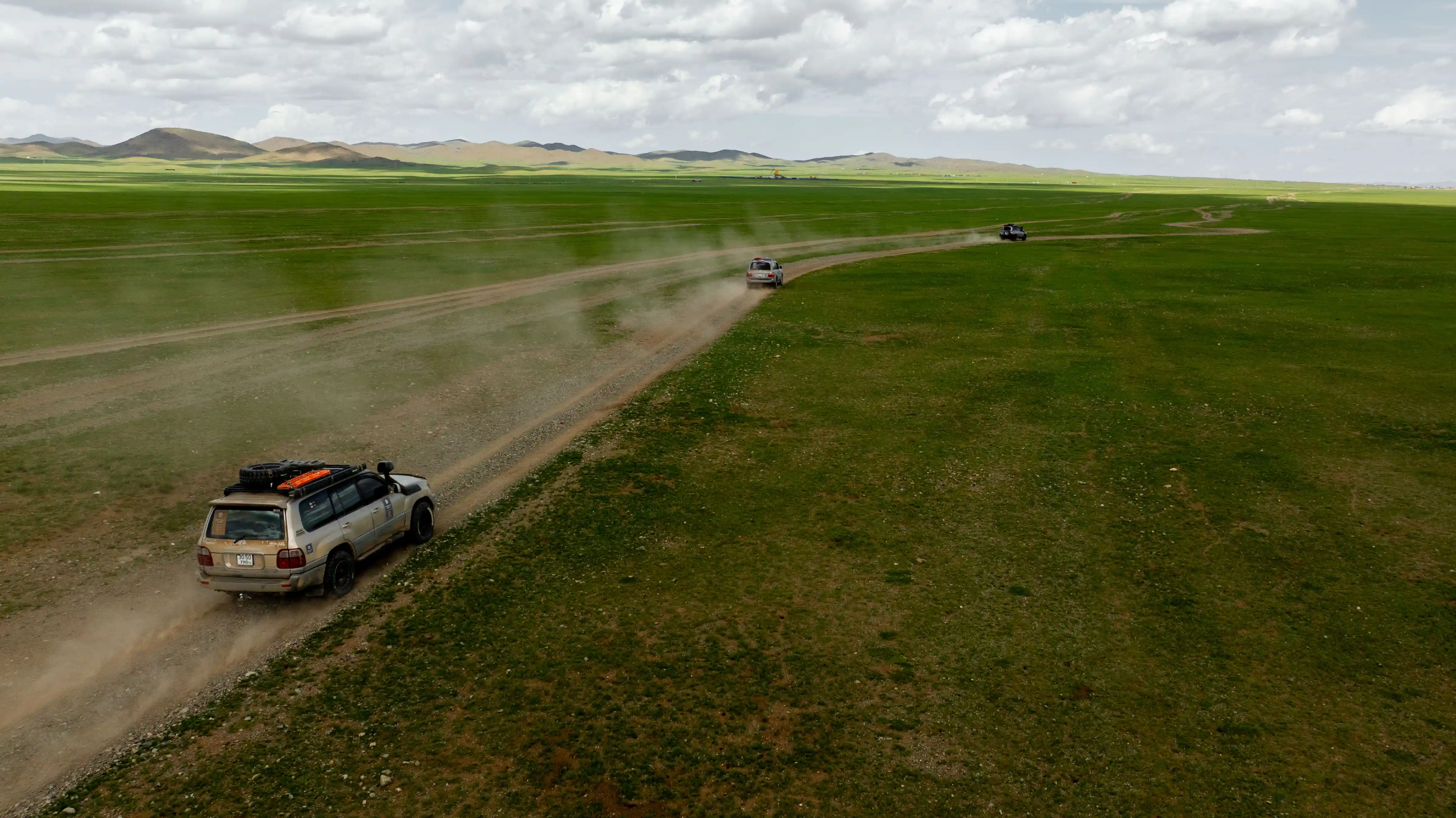 Expedition vehicles driving across the open Mongolian steppe beneath dramatic skies during a Nomadic Road overland journey