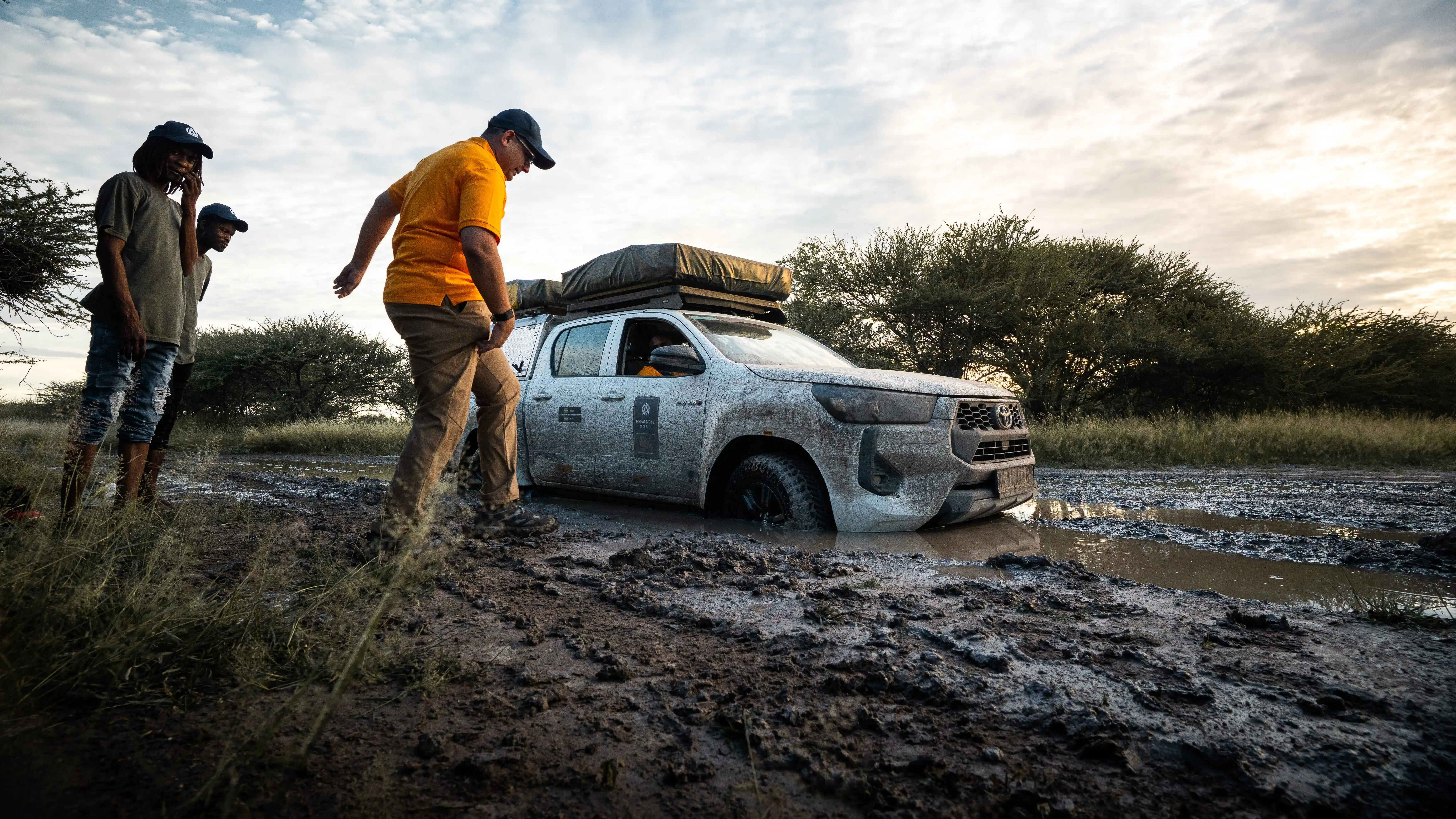 An off-road expedition truck Navigating deep mud terrain during a Nomadic Road safari with guides assisting the driver.