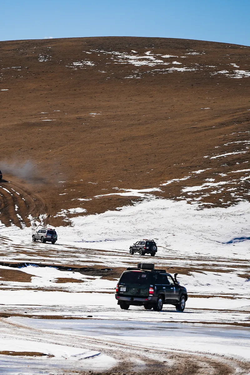 Land Cruisers crossing snow-patched hills towards Khyargas Lake, Mongolia
