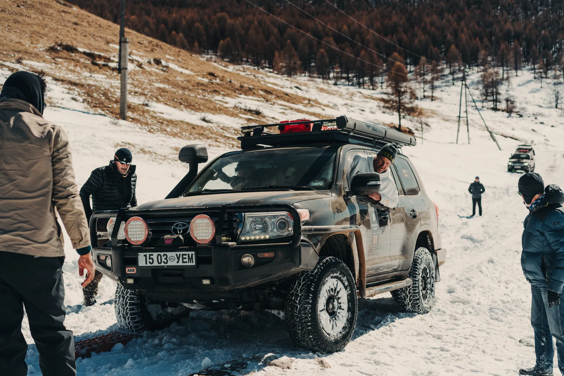Explorers gathered around a Land Cruiser on a snowy hillside, Mongolia