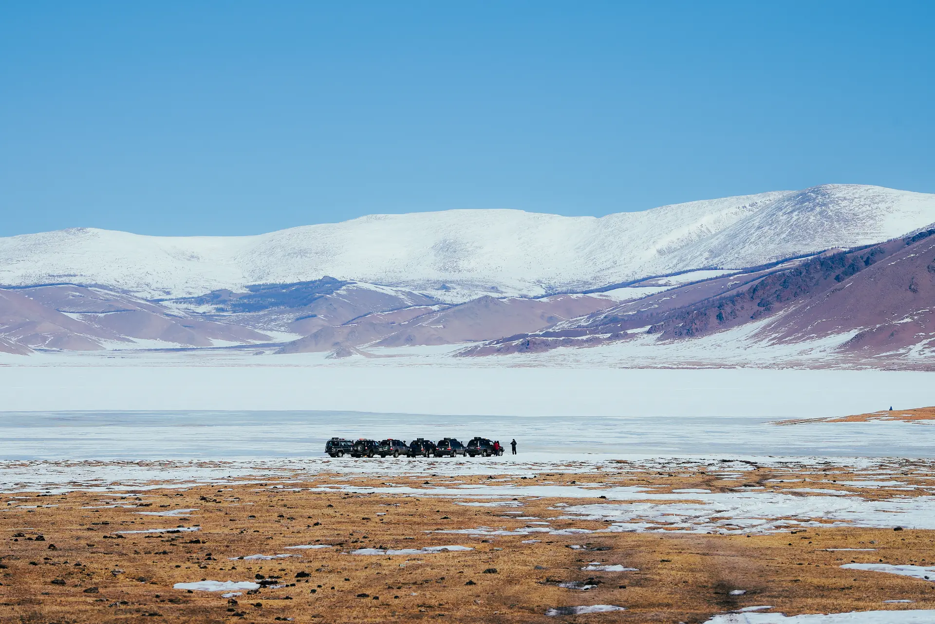 A convoy crossing a frozen lake below the snow-capped Altai, Mongolia