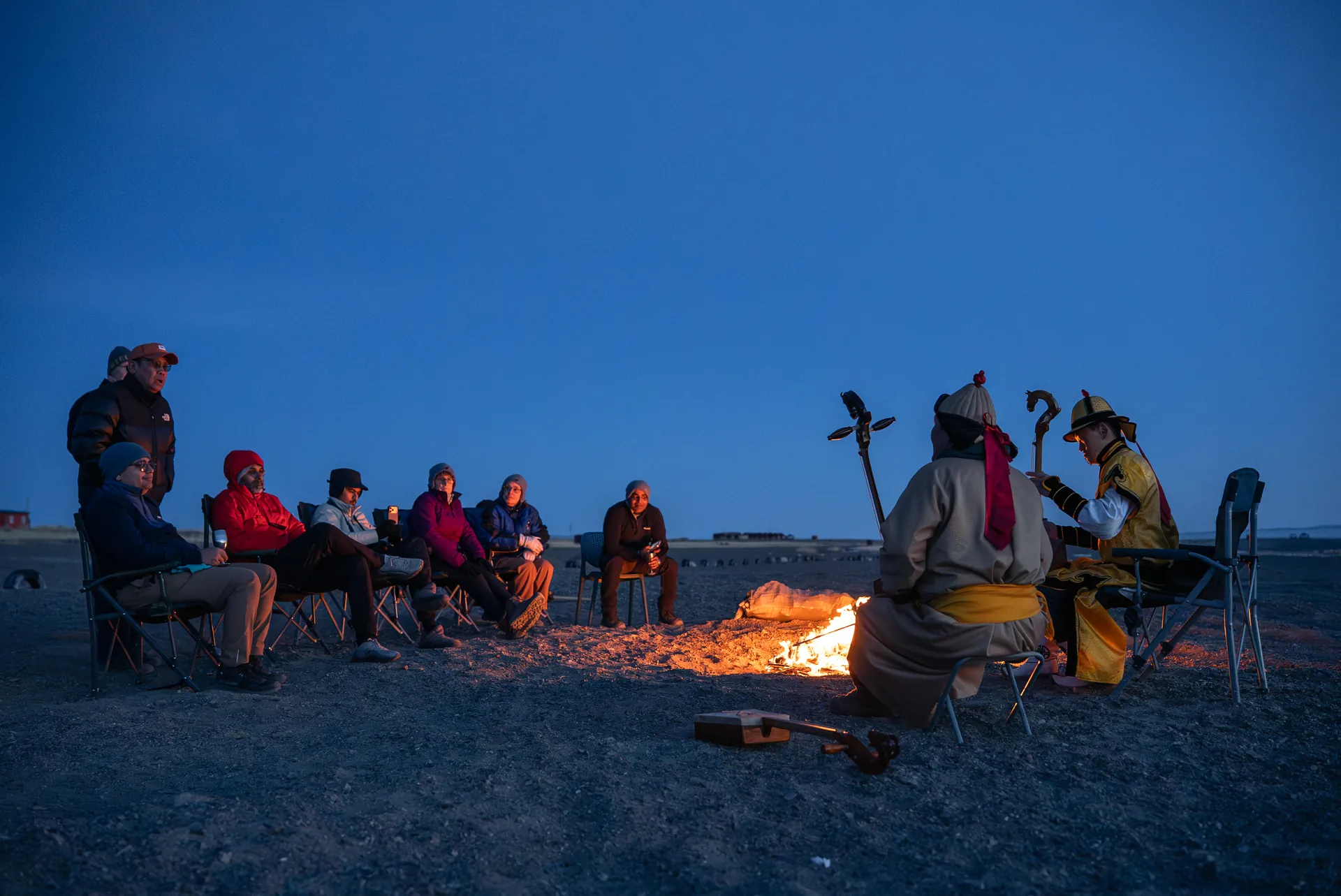Explorers around a fire at dusk with local musicians, Mongolia
