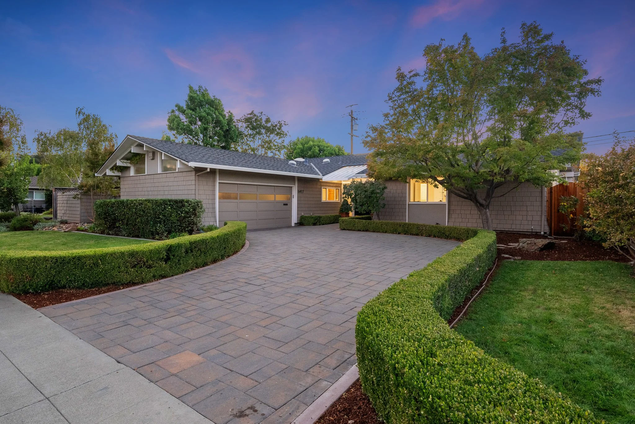 A two-story white family home in Sunnyvale, California with a green lawn, large trees, and a three-car garage