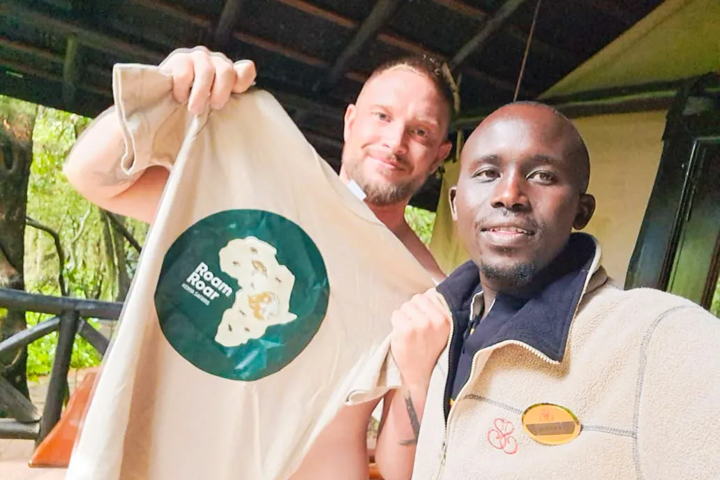 Two men smiling at the camera, one holding a beige t-shirt with a RoamRoar T-shirt
