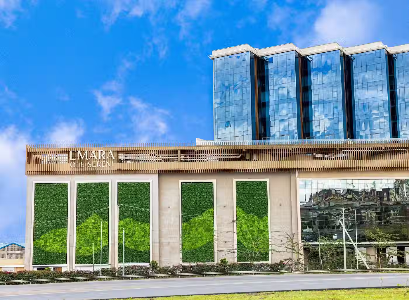 Modern commercial building with reflective glass windows and green vertical garden panels under a clear blue sky.