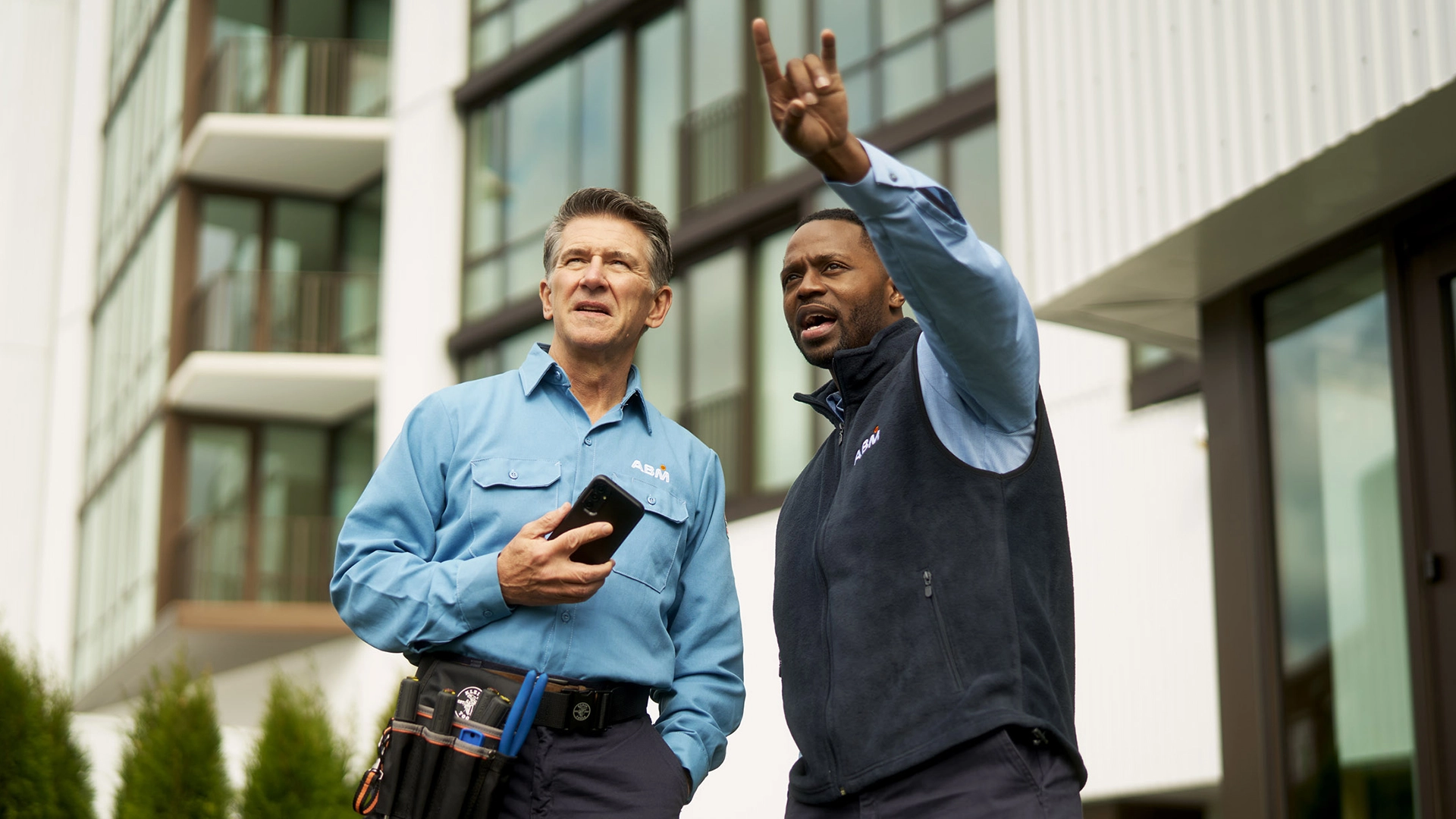 Two men in ABM uniforms standing in front of a building looking at something ahead of them