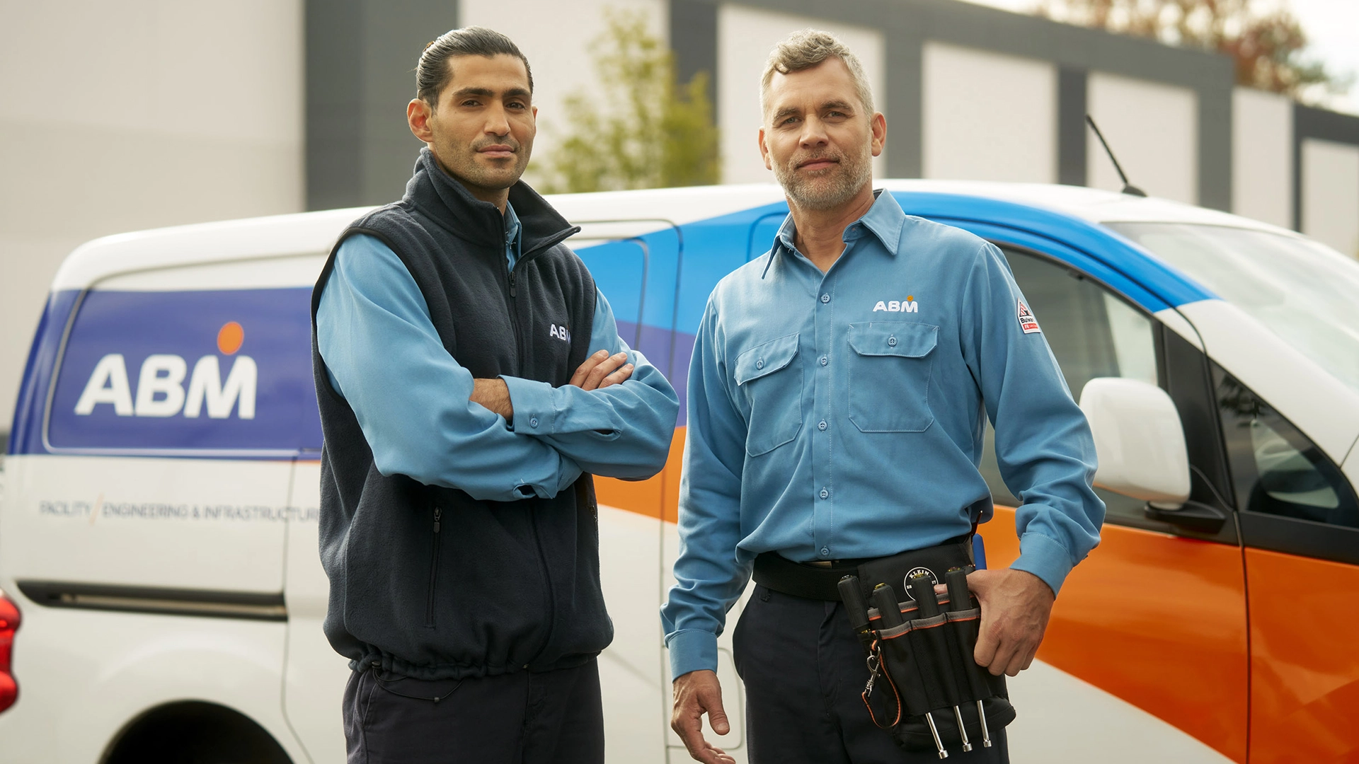 Two men in ABM uniforms standing in front of an ABM van, posing