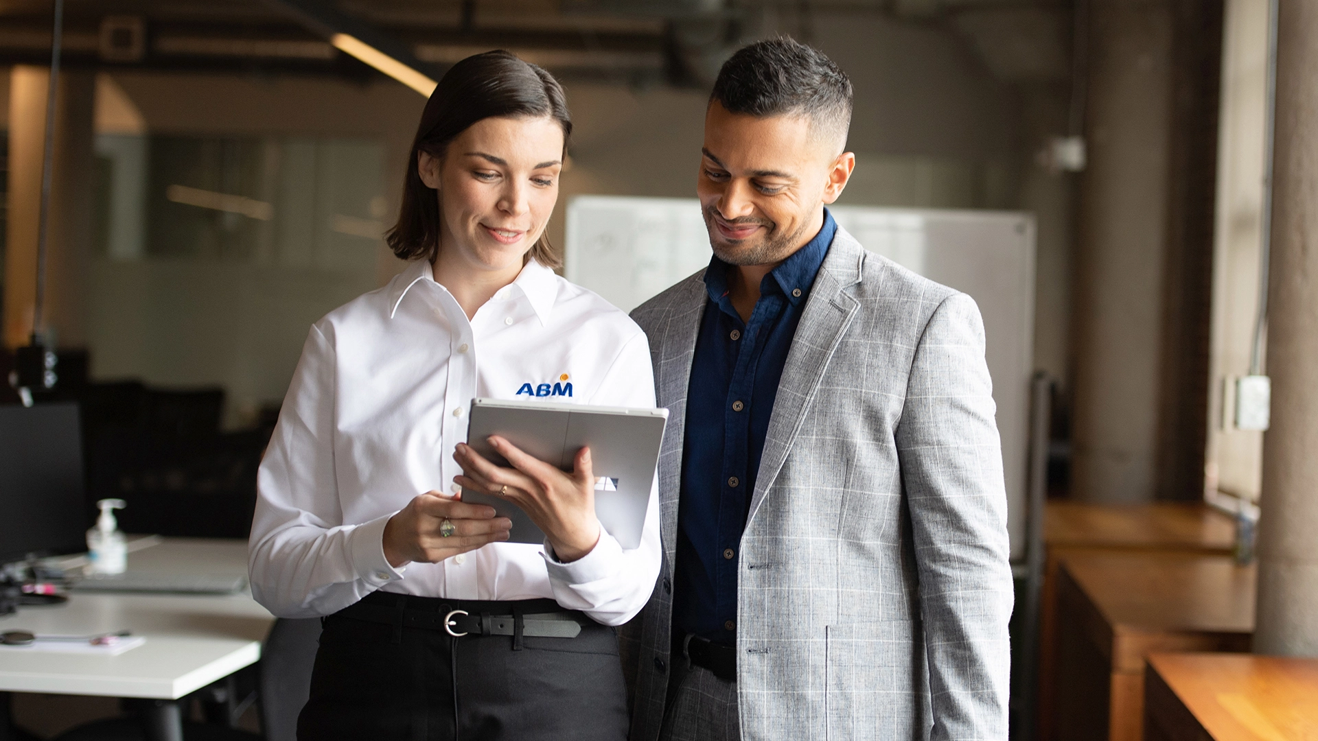 A woman wearing an ABM shirt showing a man something on a tablet