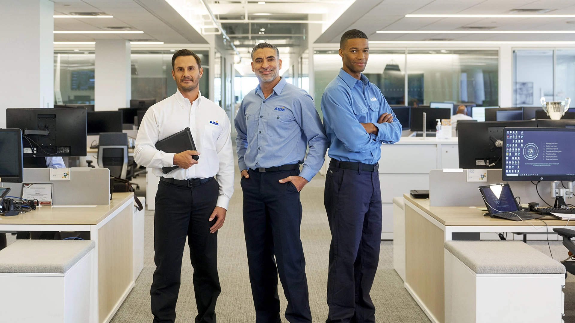 Three men in ABM uniforms standing together in an office