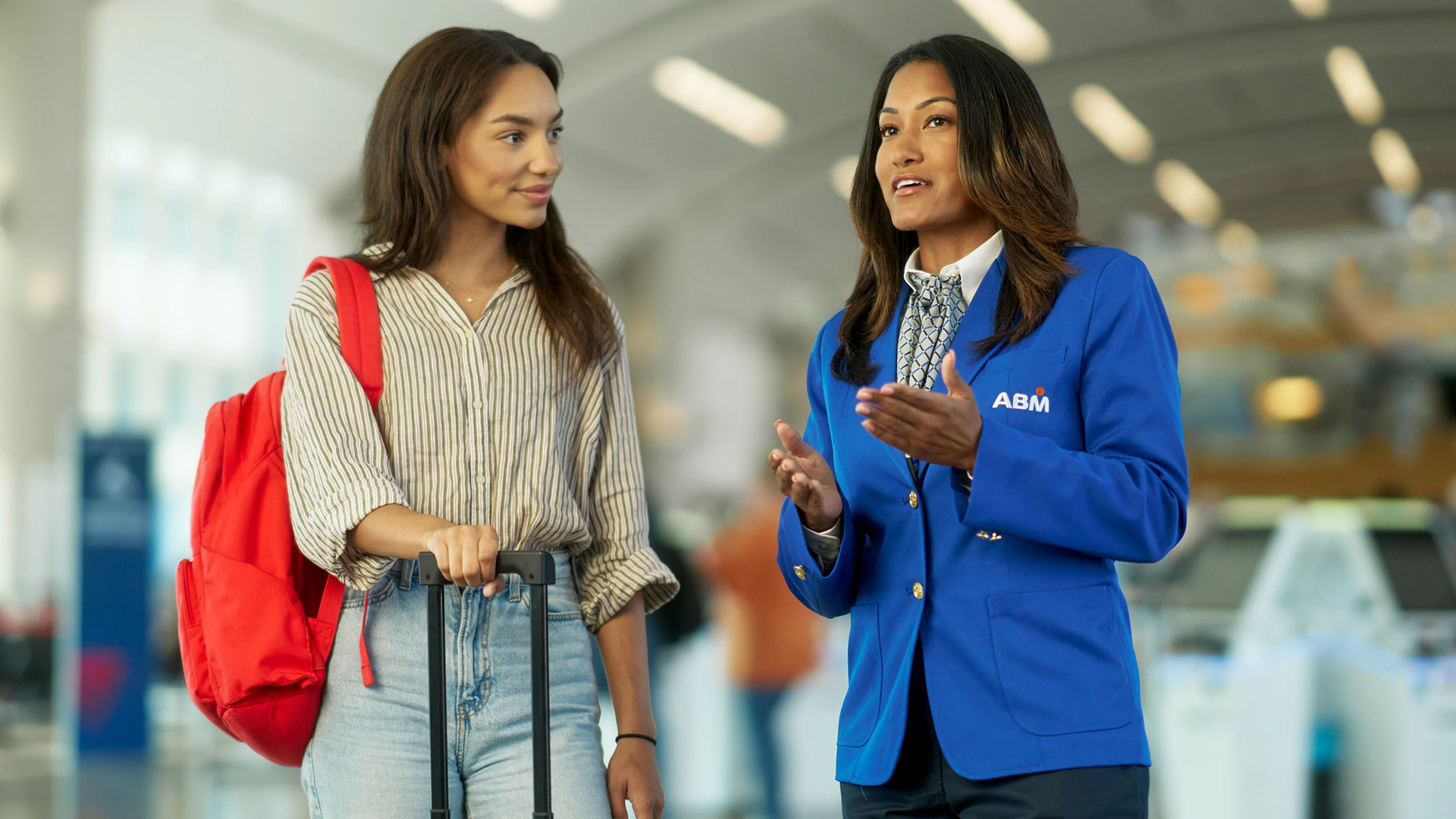 A person in an ABM uniform talking to another person holding luggage inside of an airport