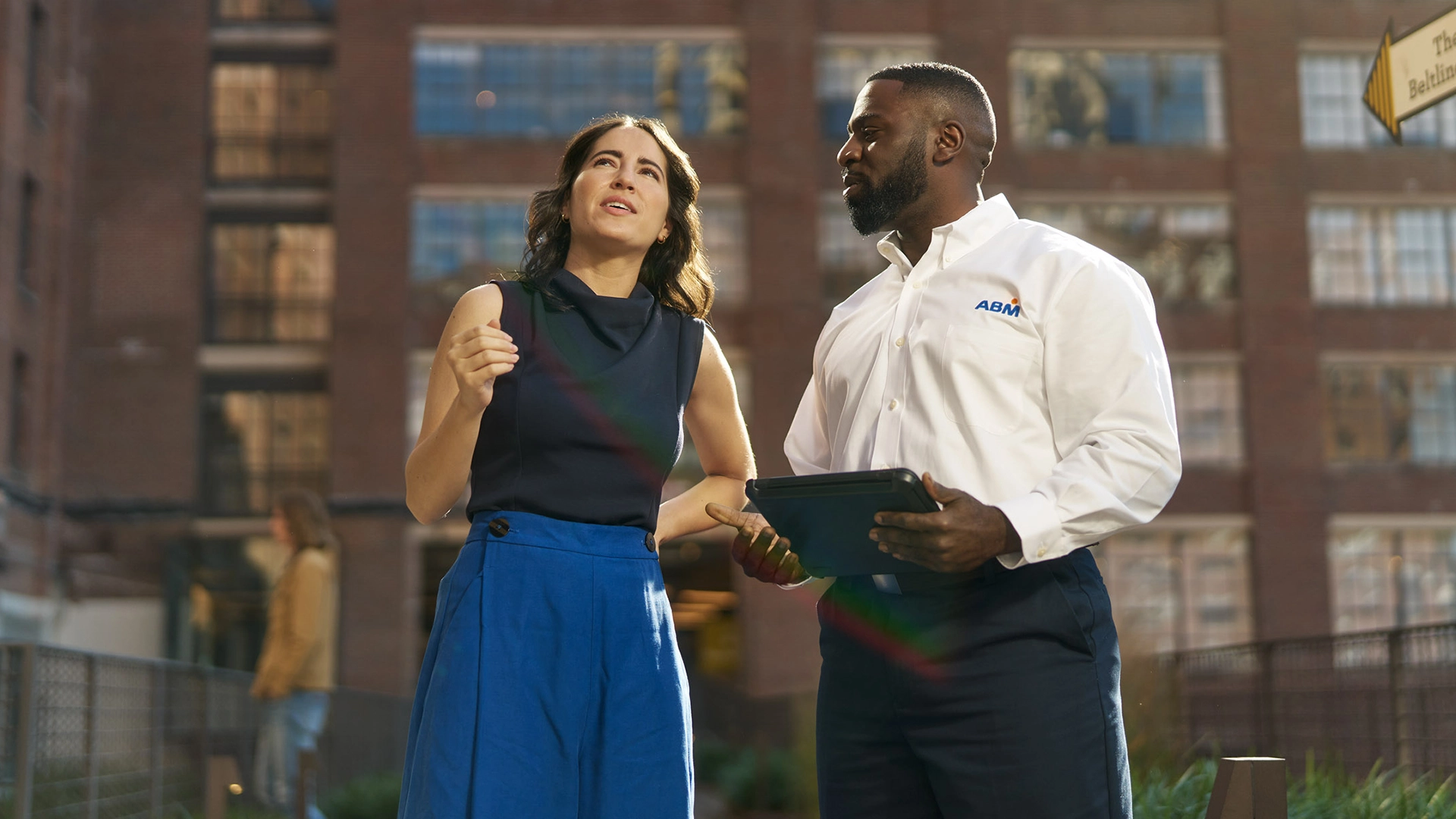 Two people having a conversation outside in front of a brick building, one in an ABM collared shirt