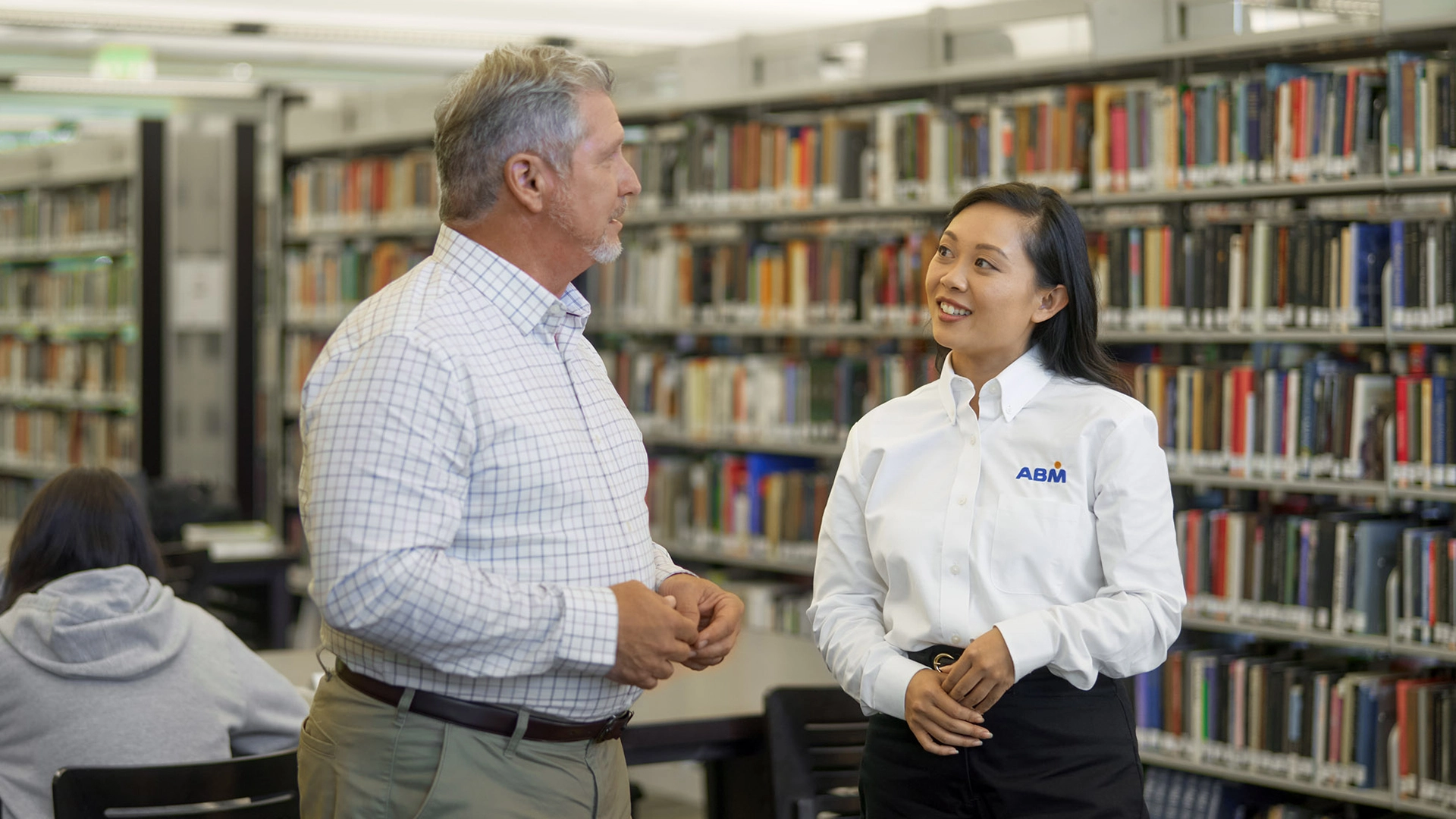 Two people speaking in a library in front of several shelves of books