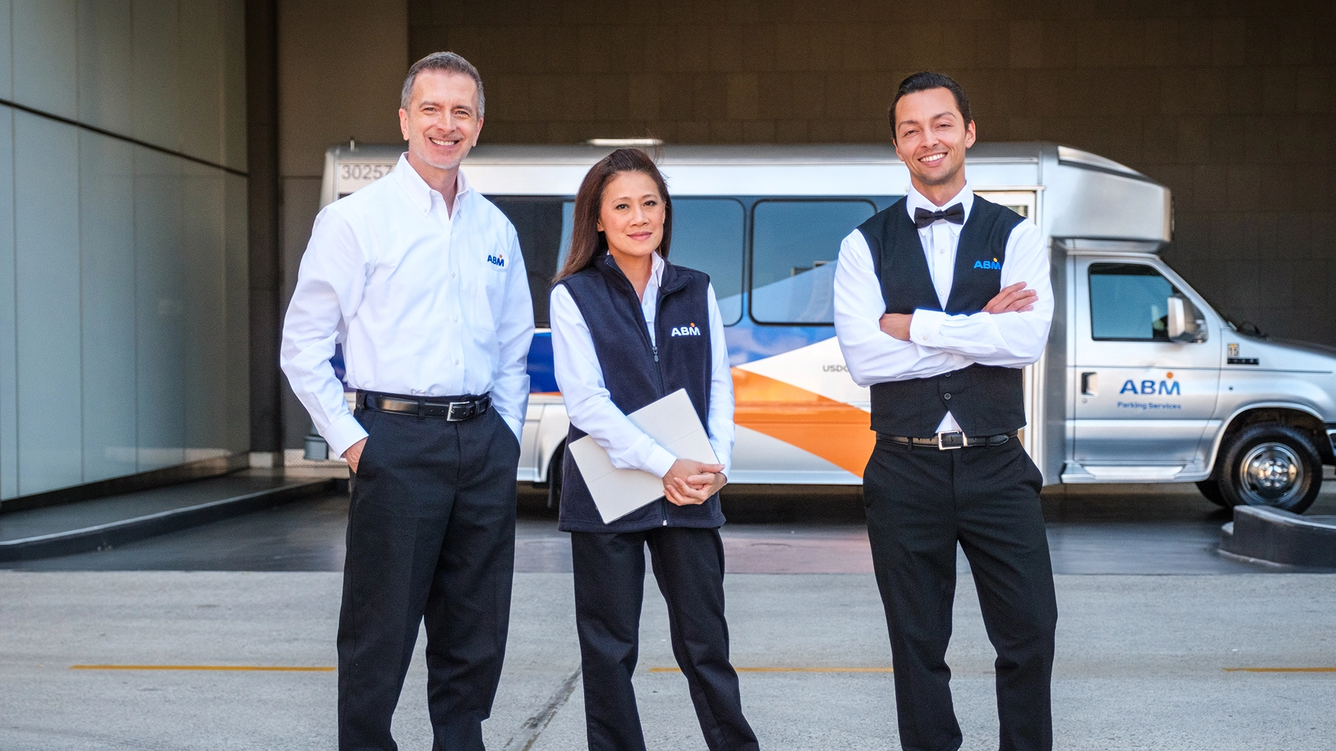 Three people standing outside in front of an ABM shuttle, smiling at the camera