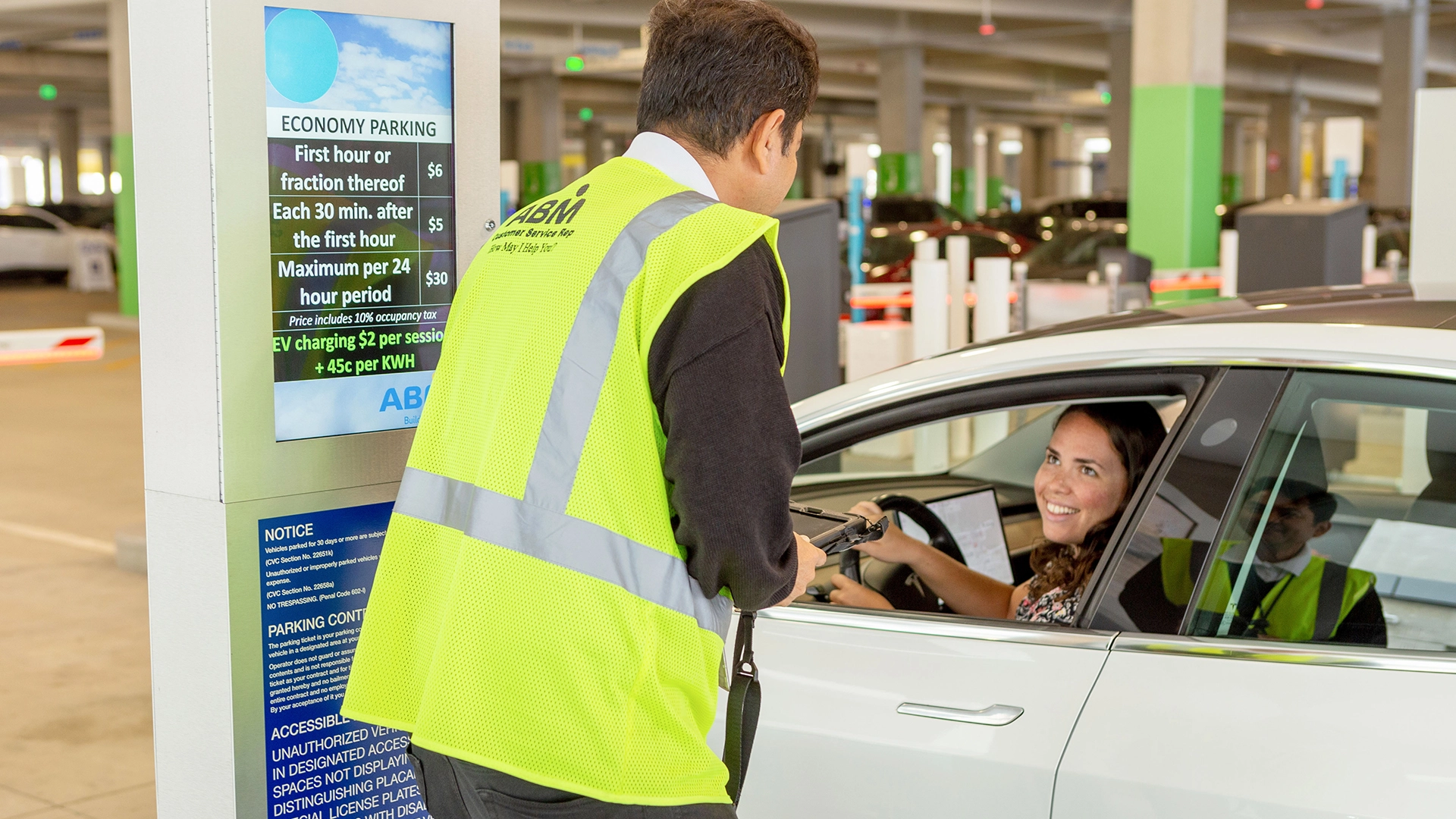 A person in a reflective vest talking to a person in a car inside of a parking garage