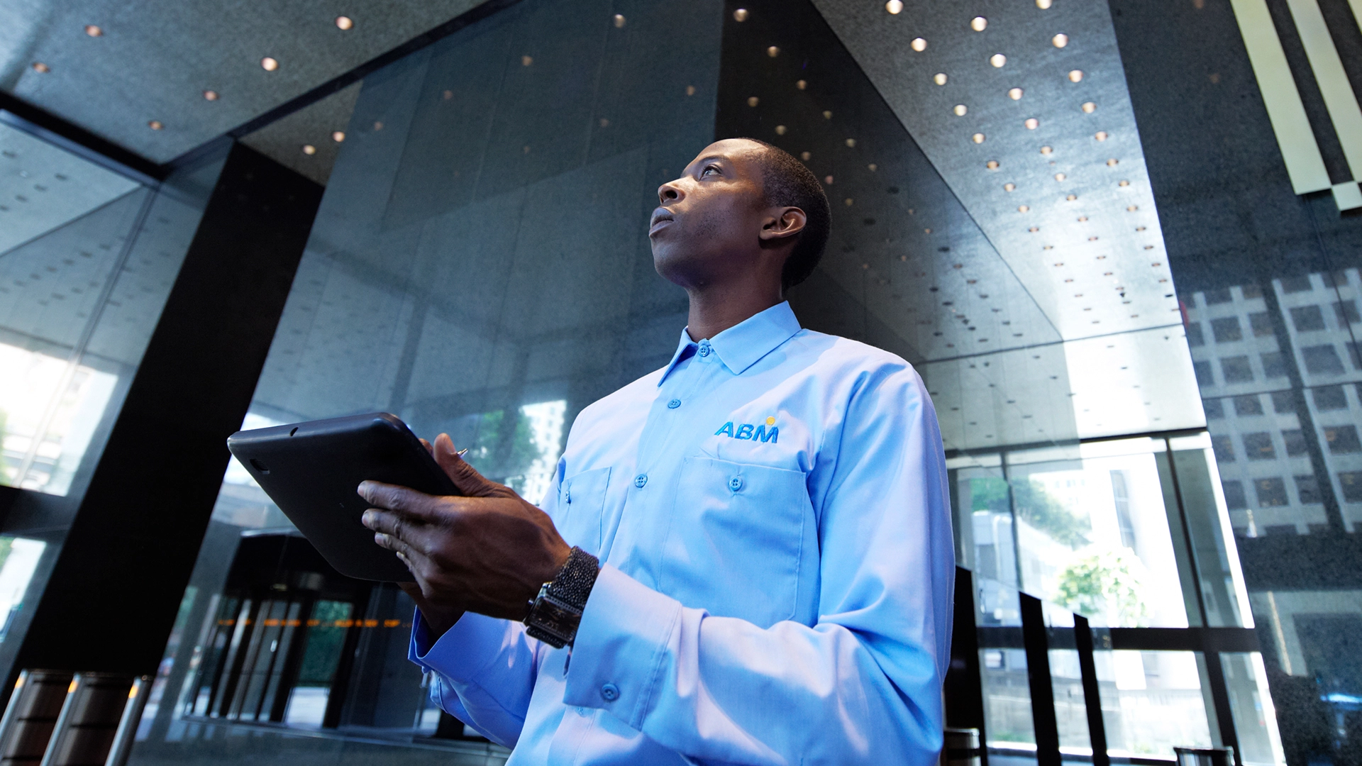 Person in an ABM shirt holding a tablet in front of a modern-looking building