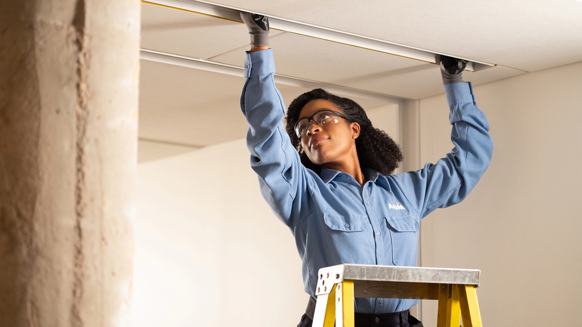 ABM employee standing on a ladder, changing out a light fixture