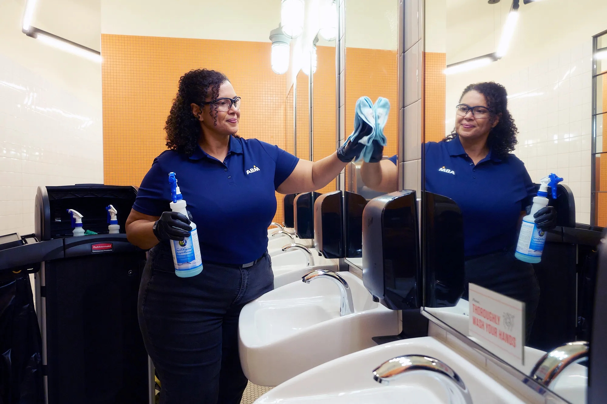 Female ABM janitorial employee cleaning a mirror