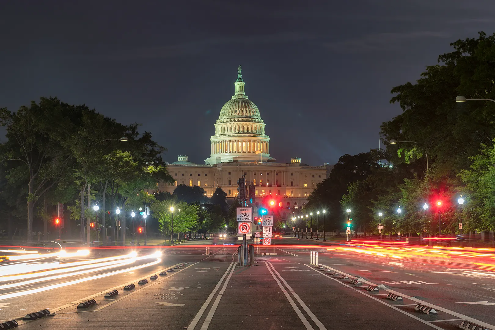 Night view of the illuminated United States Capitol building with light trails of traffic on the street in front.