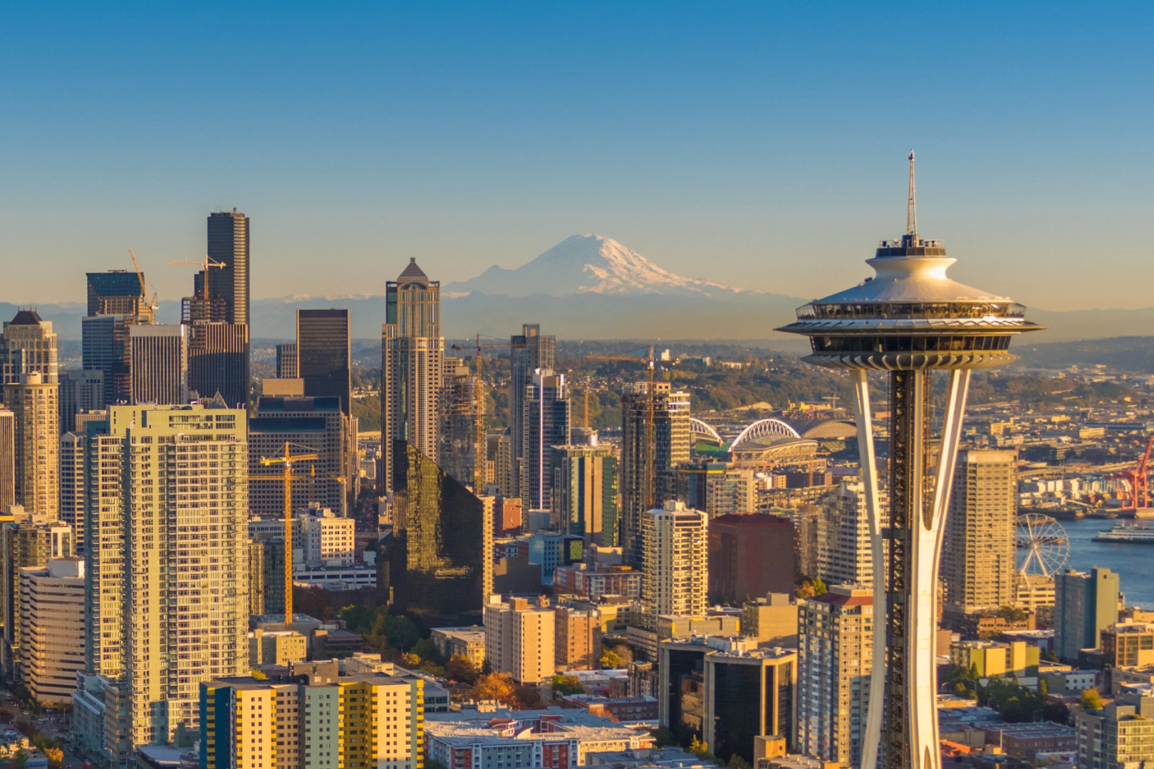Seattle skyline at sunset with the Space Needle prominently in the foreground and Mount Rainier in the background.