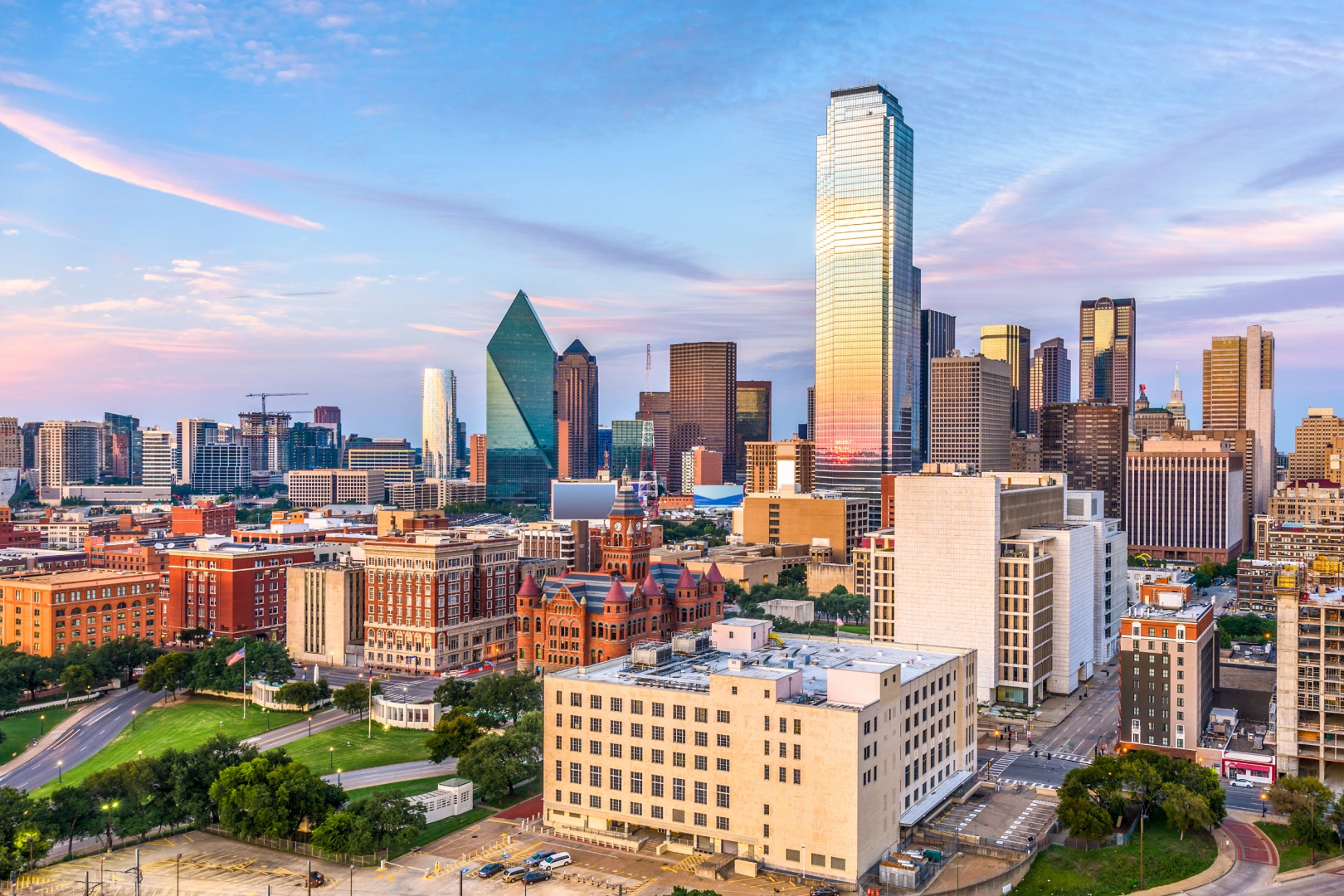 Cityscape of downtown Dallas, Texas at sunset with the tall glass skyscraper and other surrounding buildings.