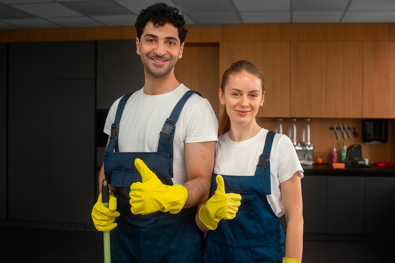 A man and woman cleaning team in overalls are giving a thumbs up.