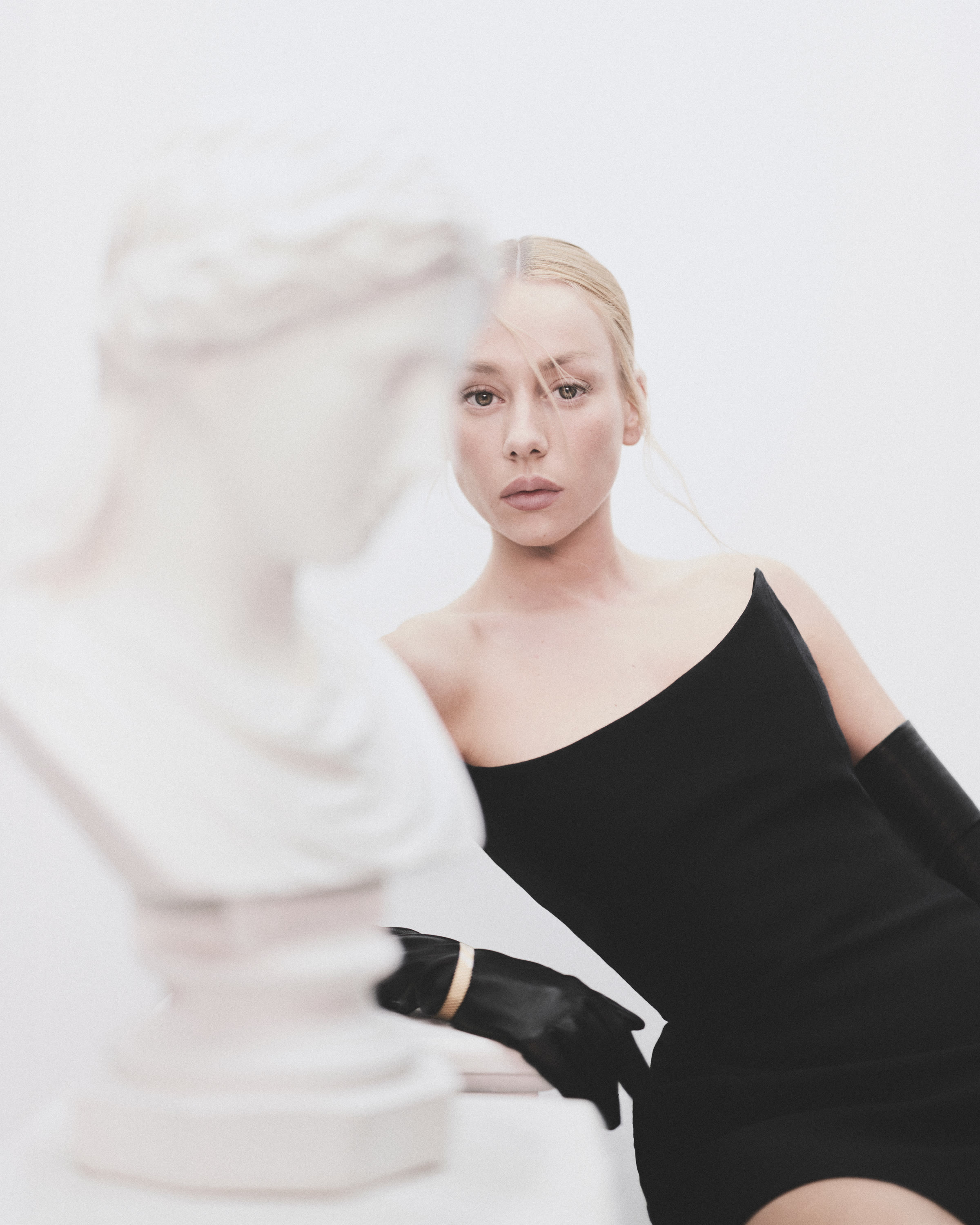 Ester Expósito in a black asymmetrical look and long glove, framed by soft white sculptural fabric.