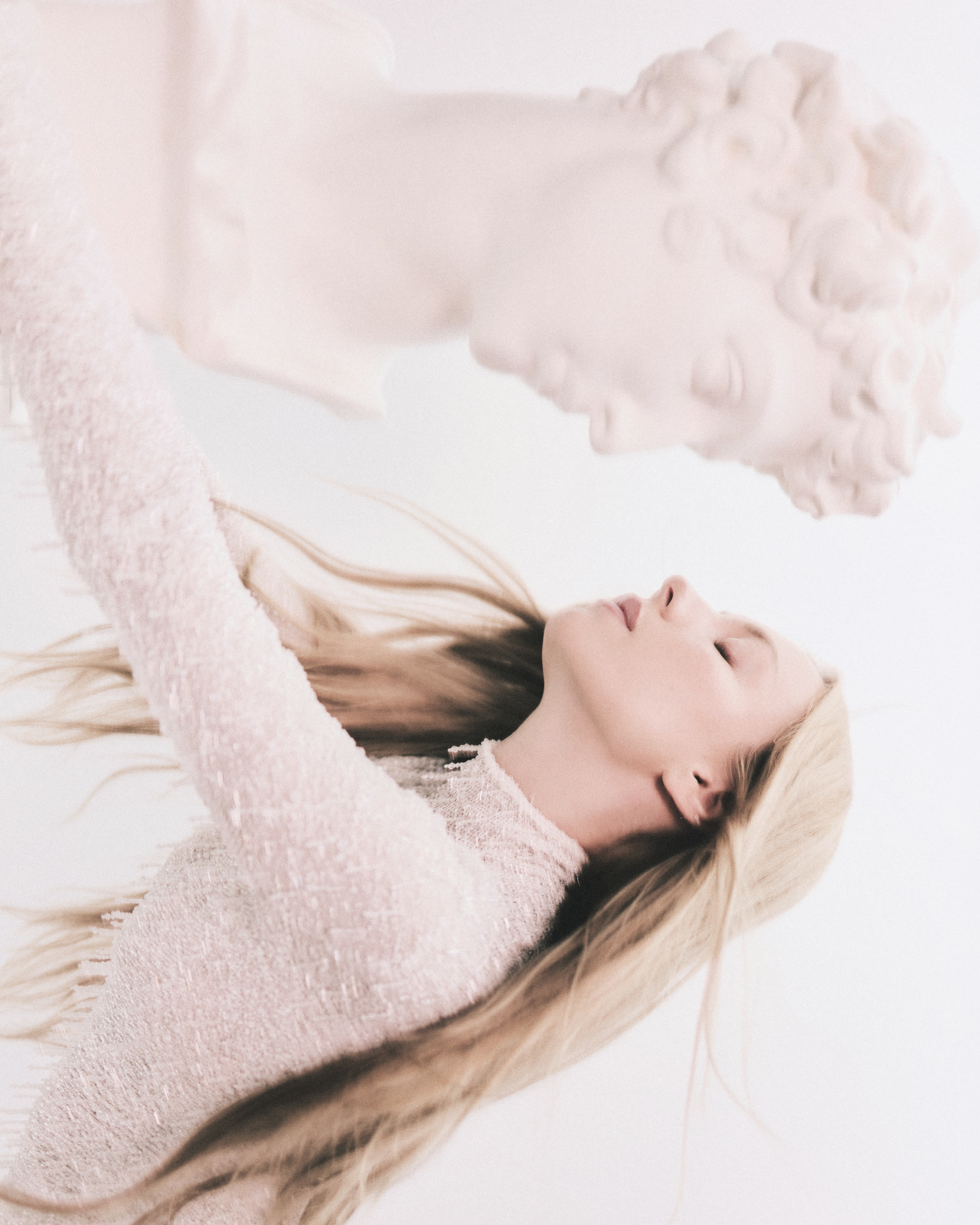 Ester Expósito reclining beside a classical bust in a pale pink textured look for Harper’s Bazaar España.