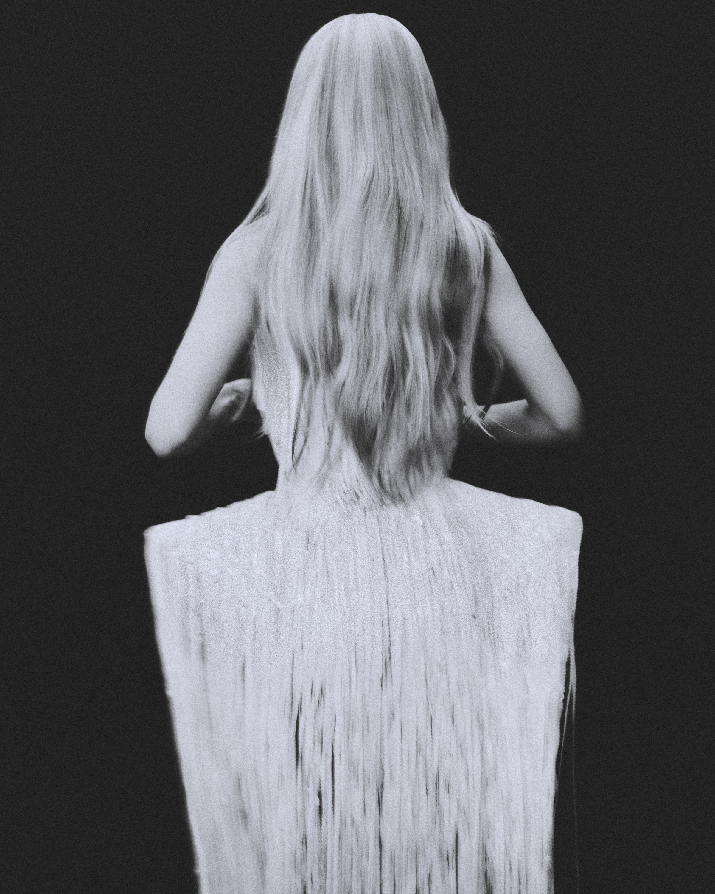 Black-and-white rear portrait of Ester Expósito in a white fringed dress, her long hair covering her face.