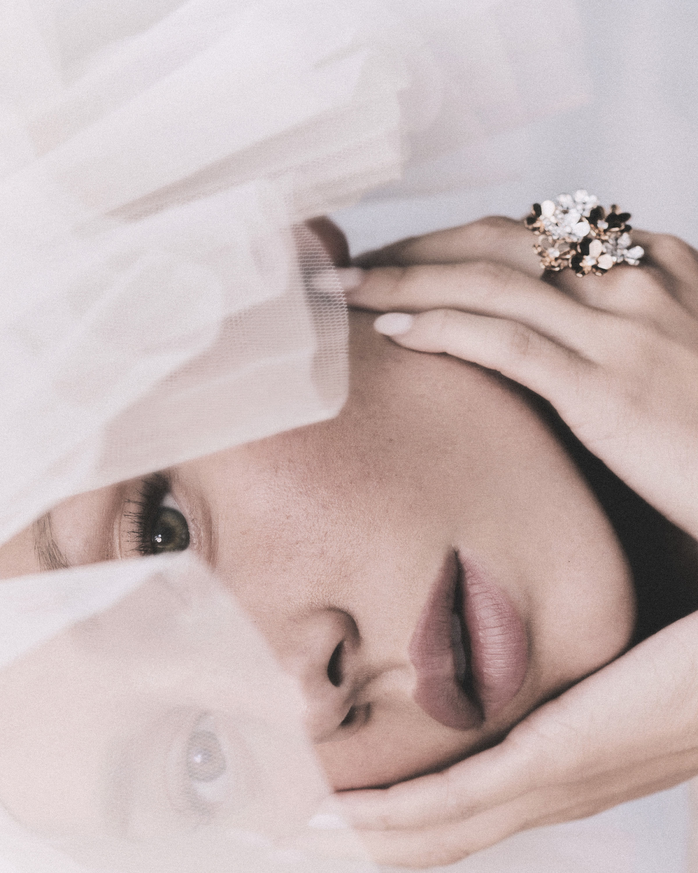 Close beauty portrait of Ester Expósito behind translucent white fabric, wearing a floral jeweled ring.