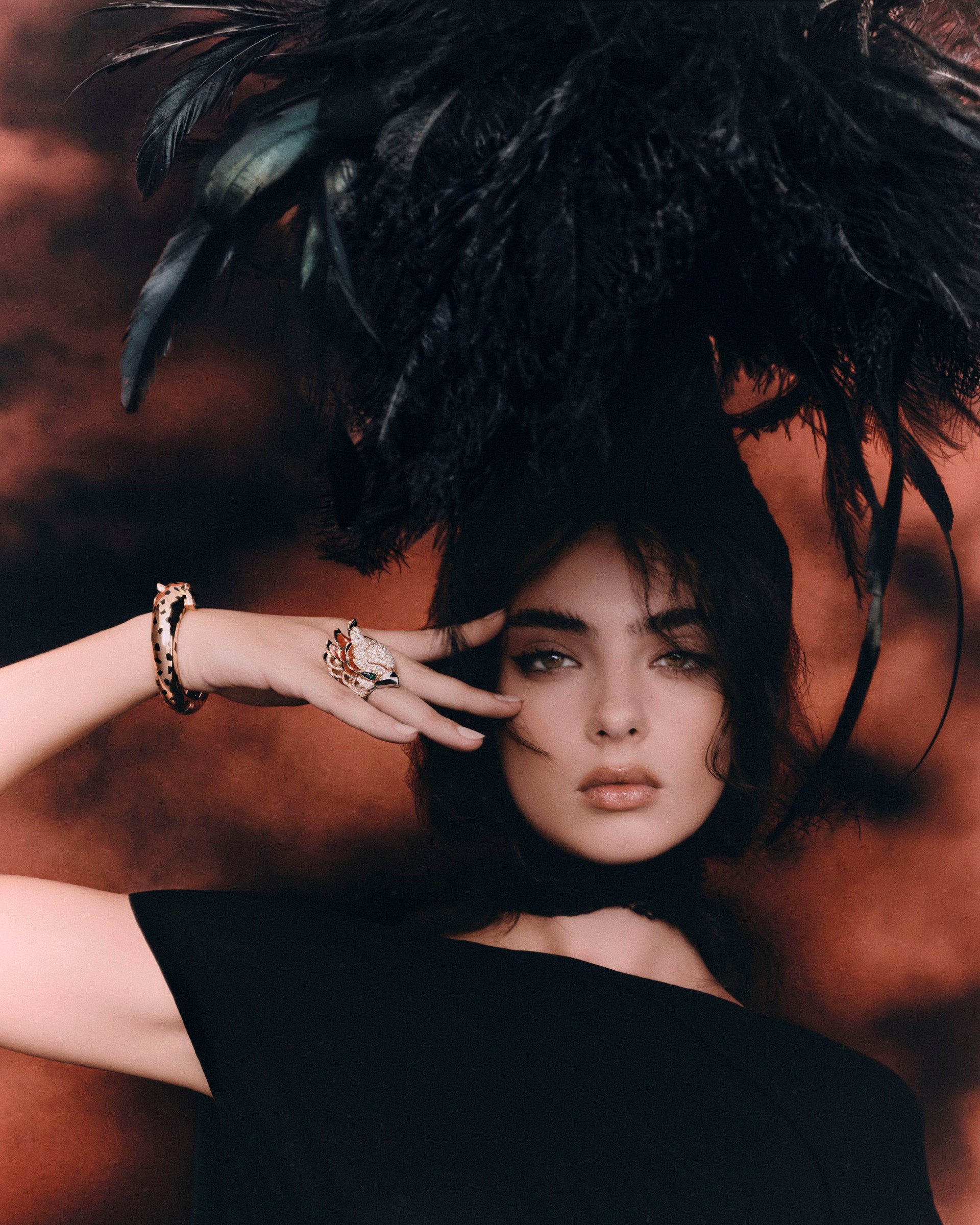 Deva Cassel in a black look with sculptural feathers, her hand framing one eye.