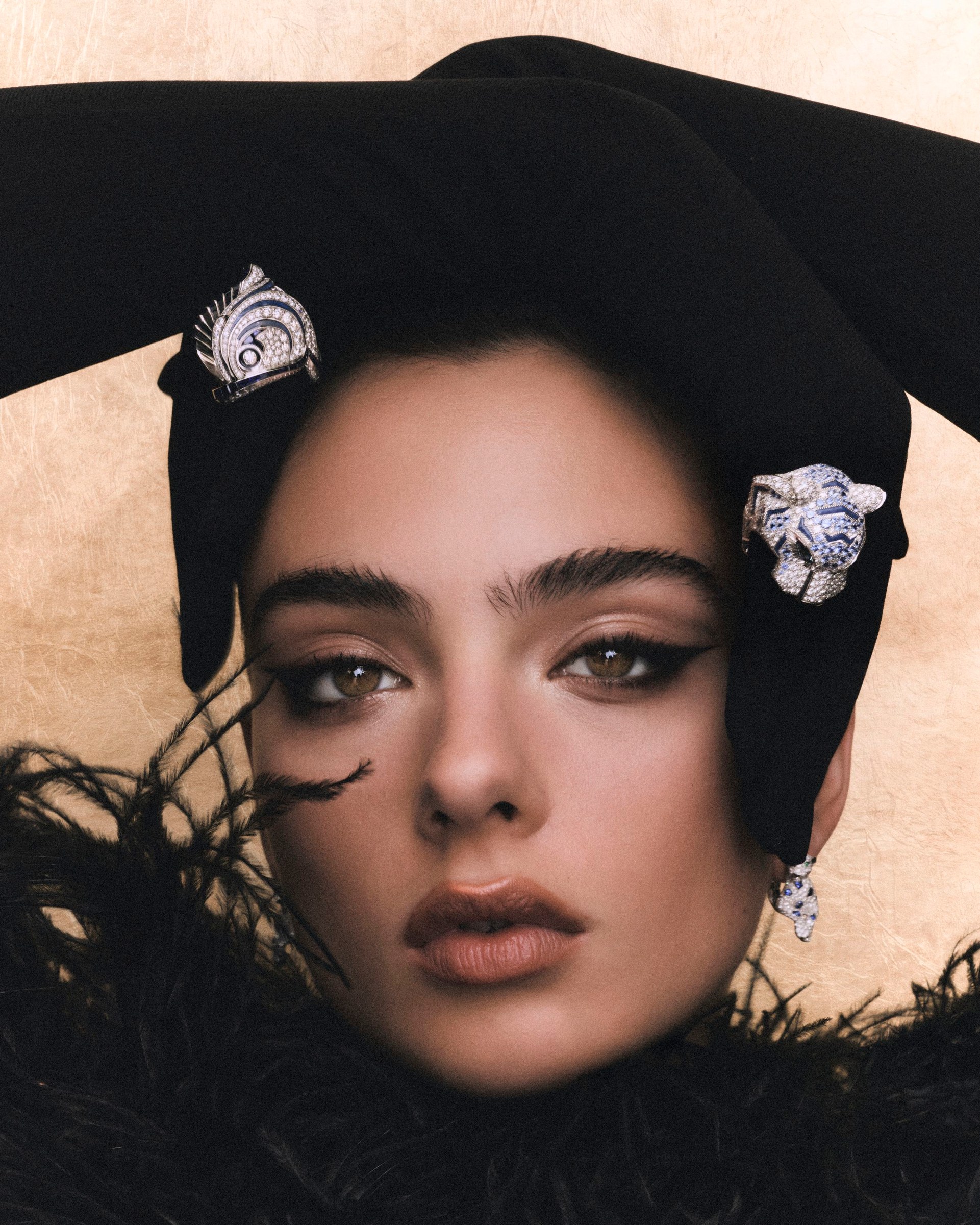 Tight portrait of Deva Cassel framed by black gloves, feathers and sculptural rings.