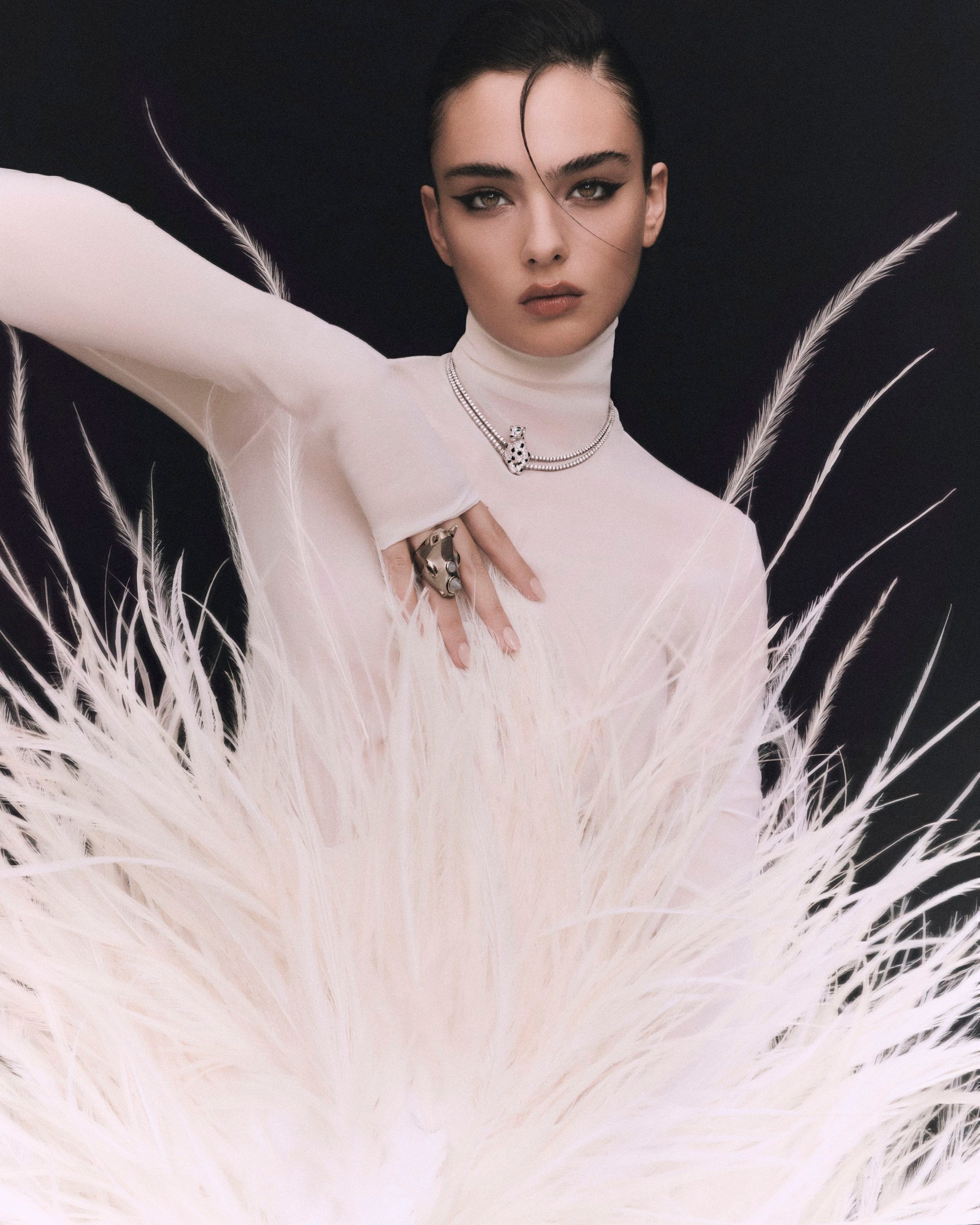 Closer framing of Deva Cassel in a pale look with one arm extended and white feathers.