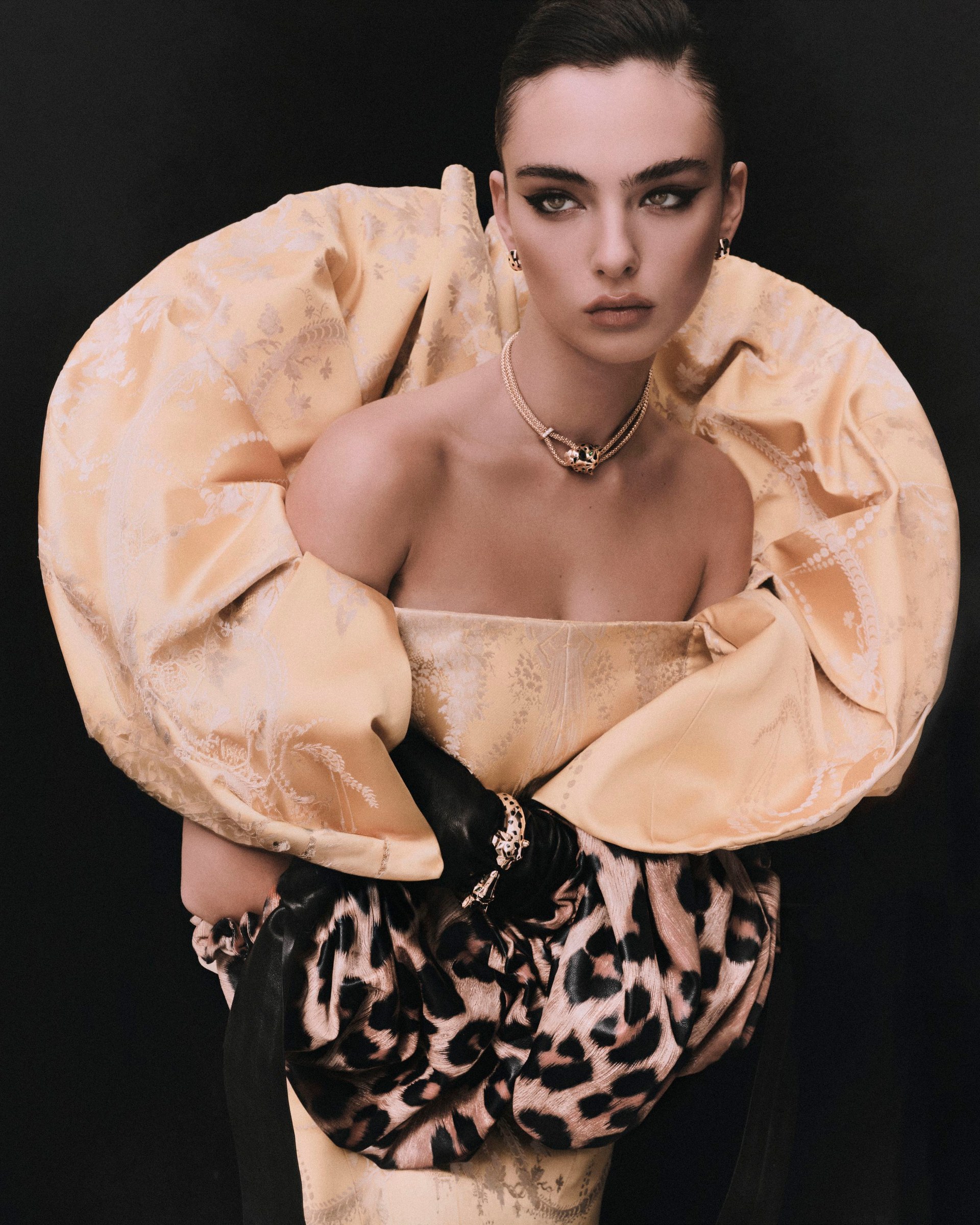 Deva Cassel in a sculptural gold-toned collar and patterned outfit against black.