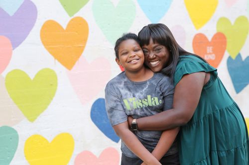 Shaunta With a Young child in front of a colorful background full of painted hearts