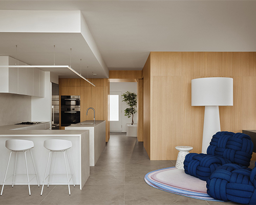 White and wood-paneled kitchen with a central island, stools, and a designer living room