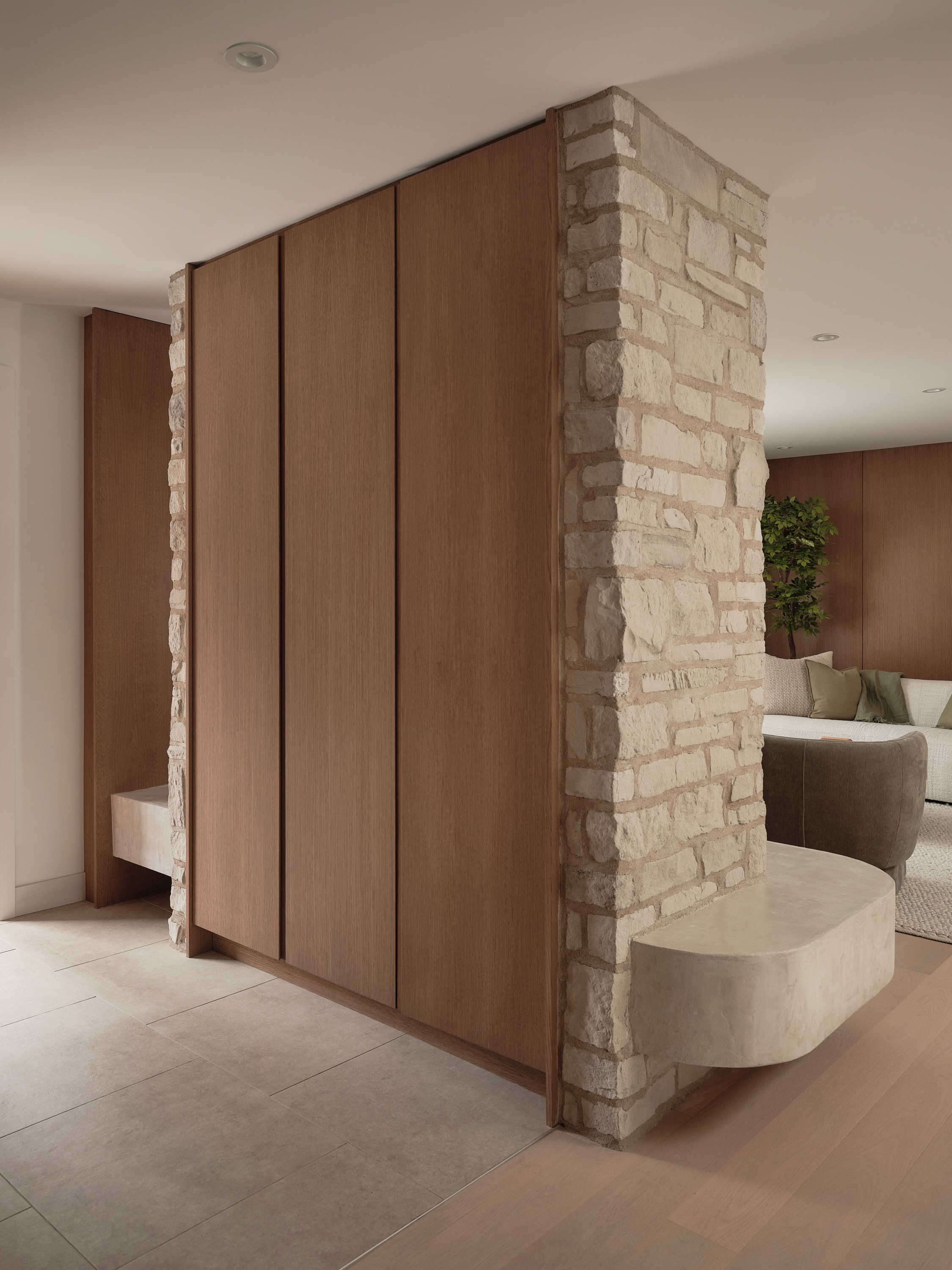 Entrance hall with a corner column made of natural stone, wooden doors, and a built-in bench; living room in the background