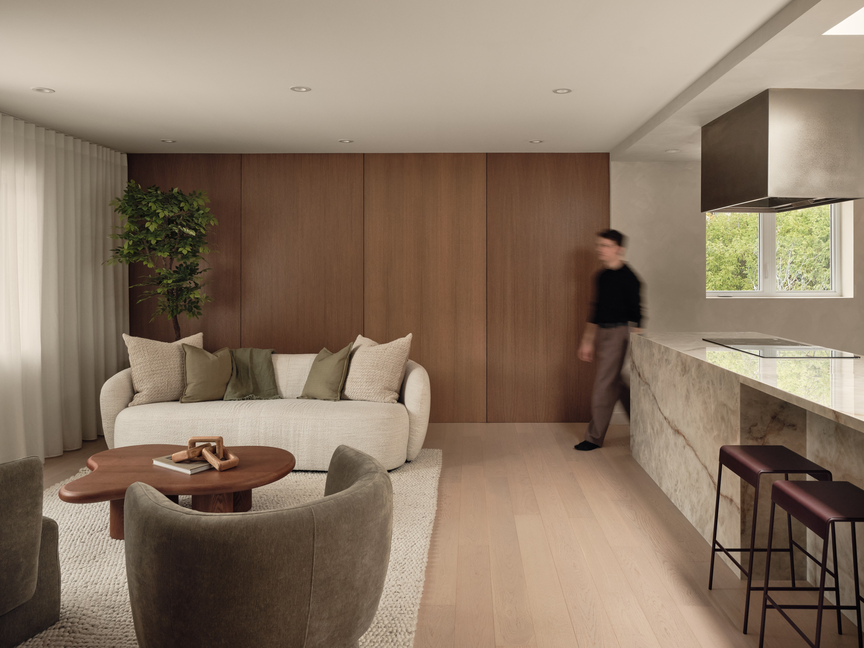 Living room open to the kitchen, featuring a beige sofa, taupe armchairs, and a veined marble island