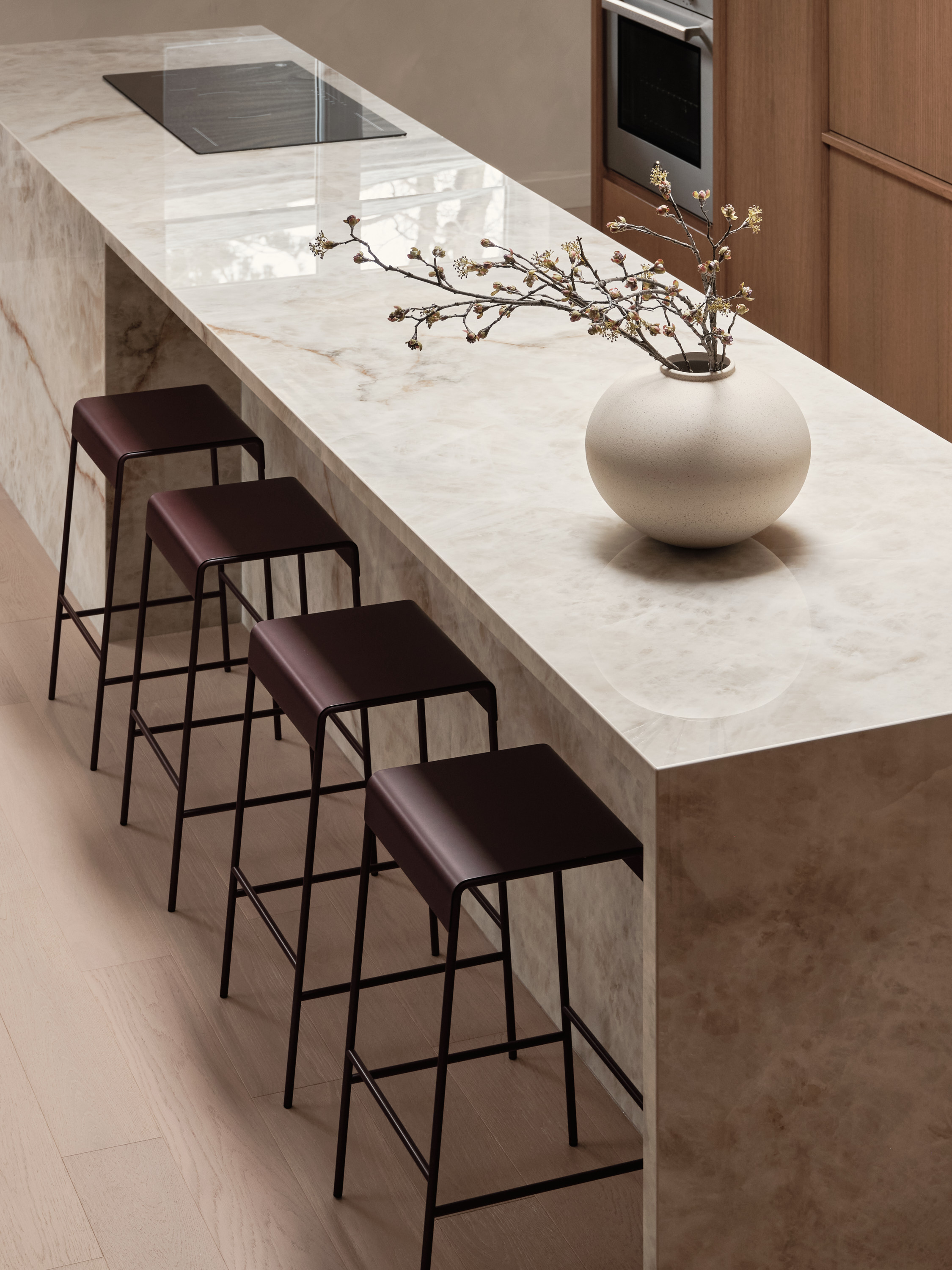 Corner of the veined marble kitchen island with burgundy leather stools and a ceramic vase