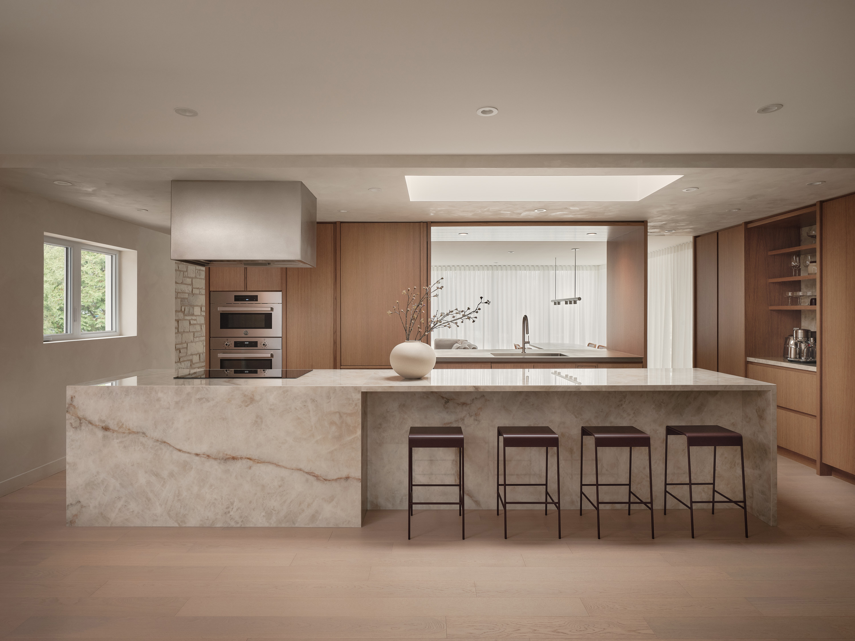 Kitchen with a veined marble island, a suspended range hood, and a white ceramic vase