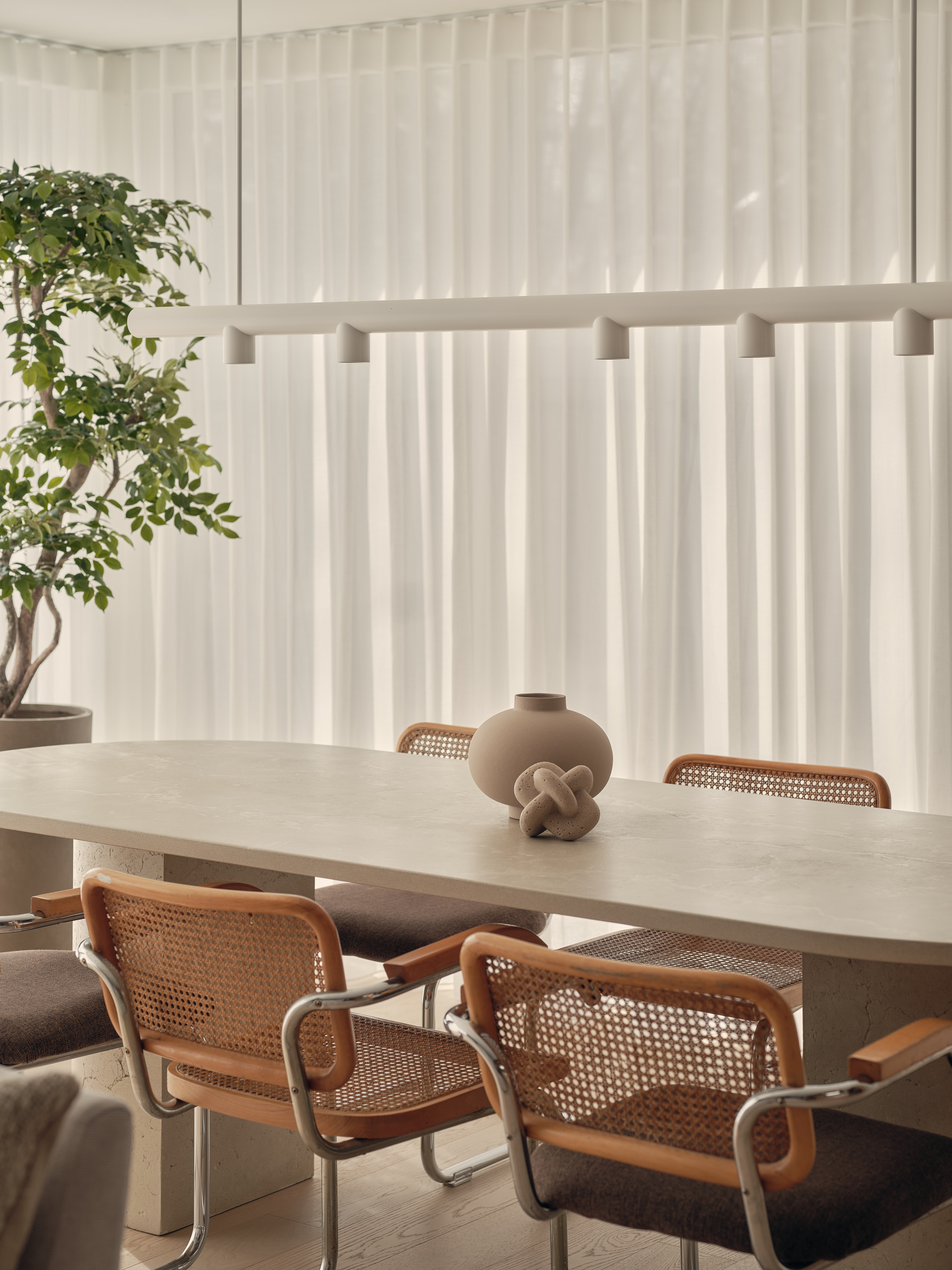 Stone dining table with a ceramic vase and a gnarled wood carving, wicker chairs