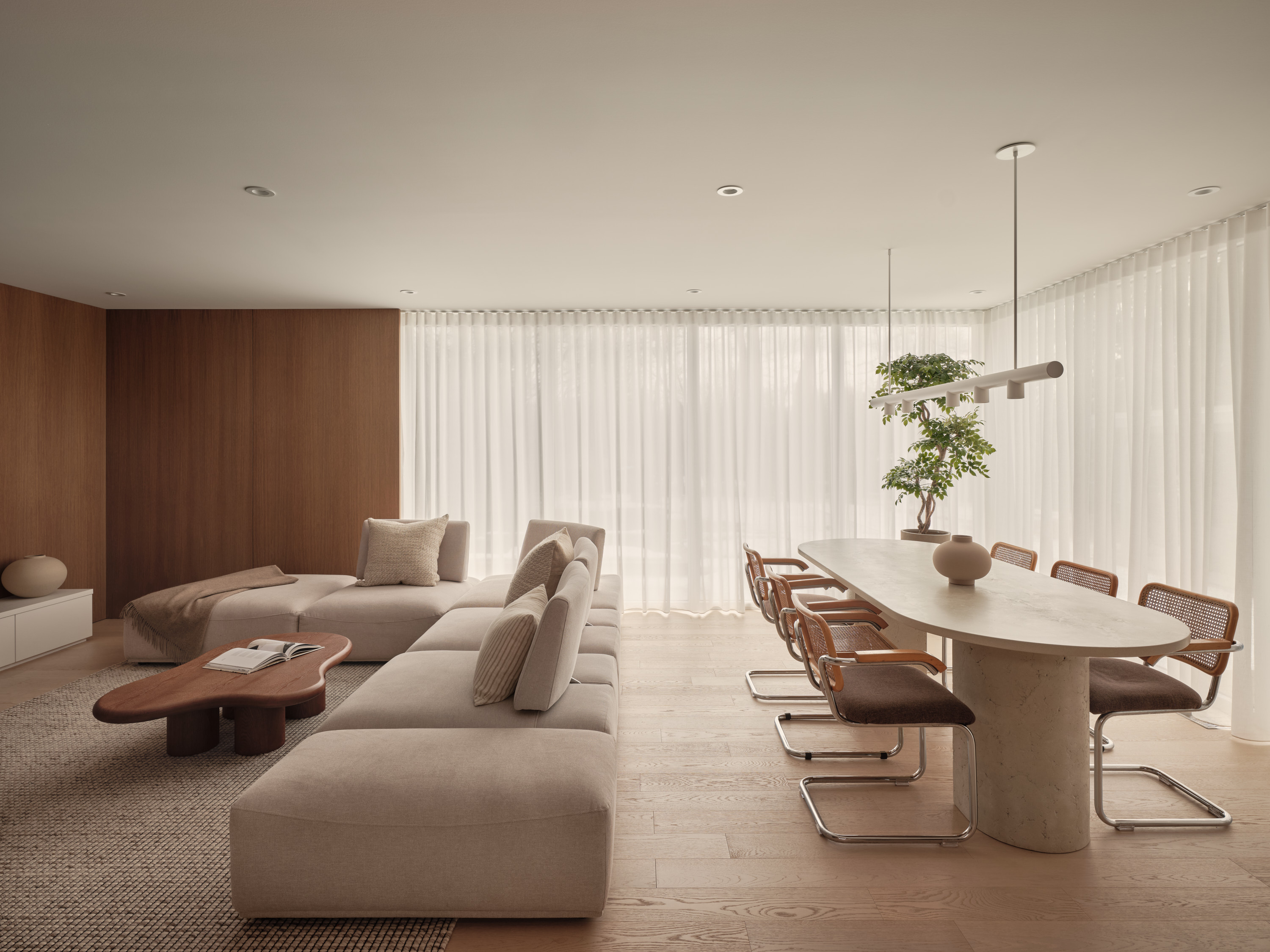 Dining room with an oval stone table, wicker chairs, and a decorative tree; living room in the background