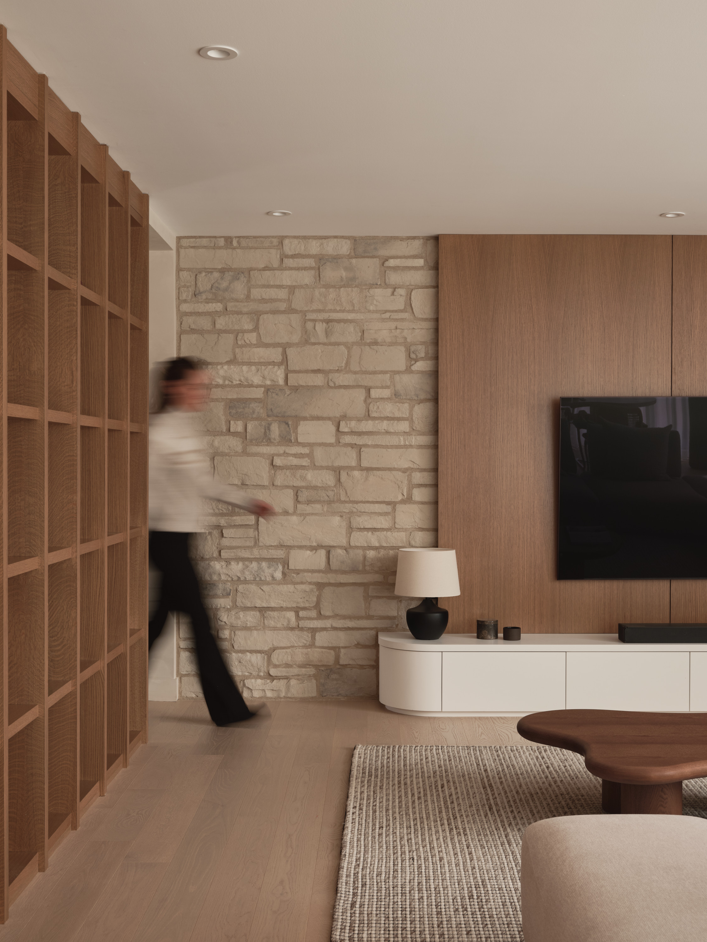 Hallway with a natural stone wall, an open bookshelf, and a living room with a TV in the background