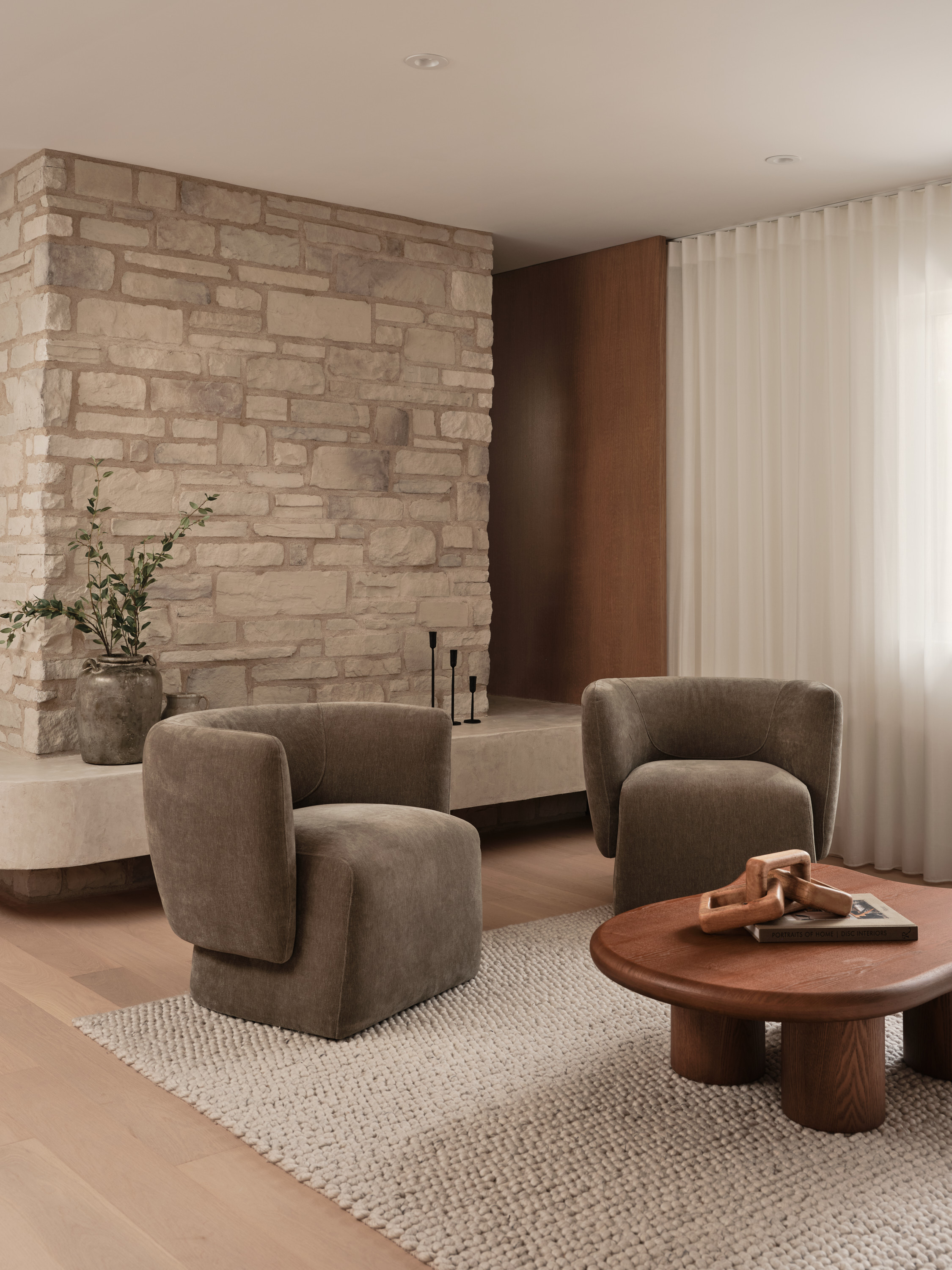 Living room with a natural stone accent wall, curved taupe velvet armchairs, and a round wooden coffee table