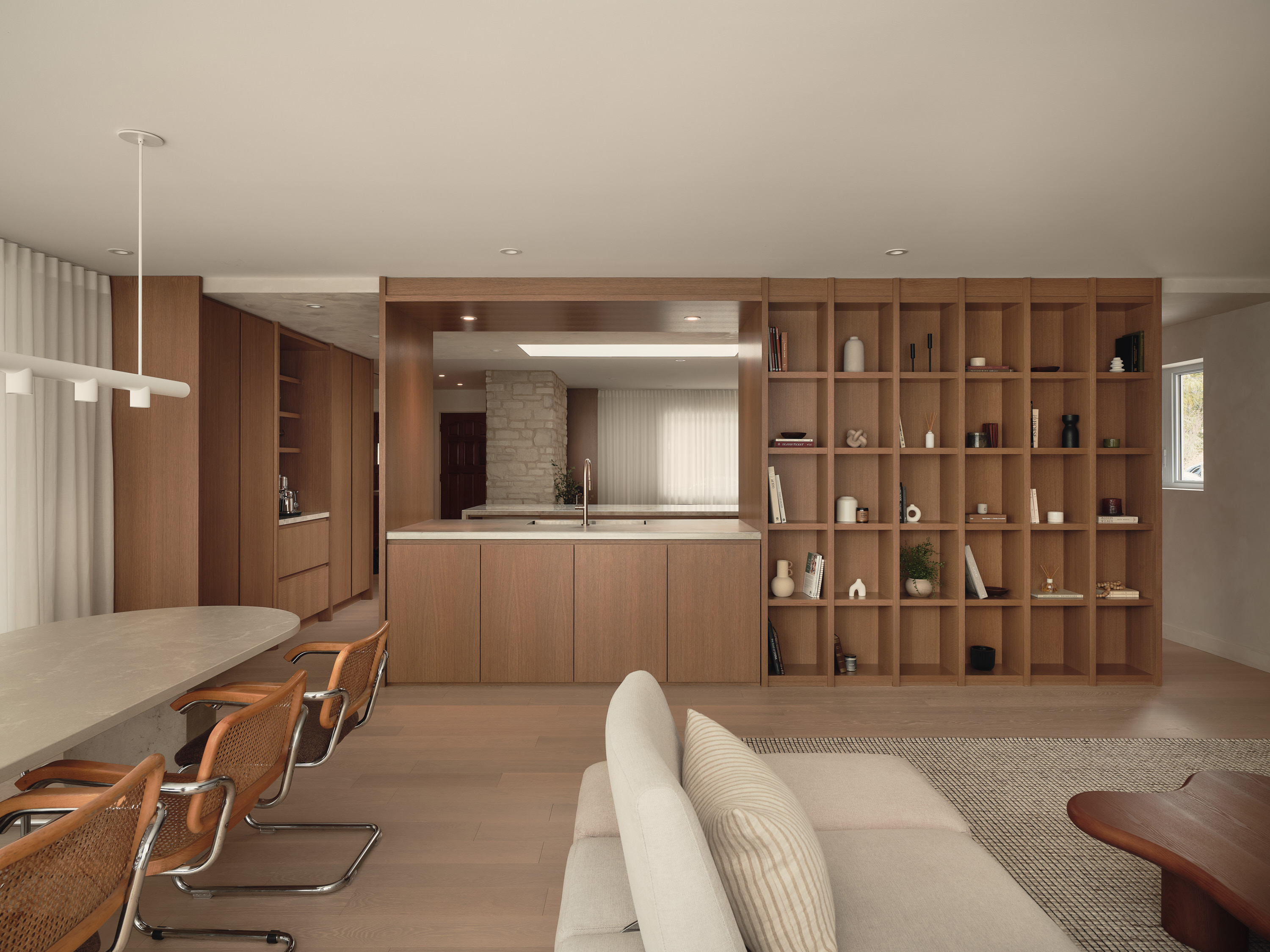 Open-concept kitchen and living room with a wooden bookshelf filled with books and decorative items, and a natural stone wall in the background